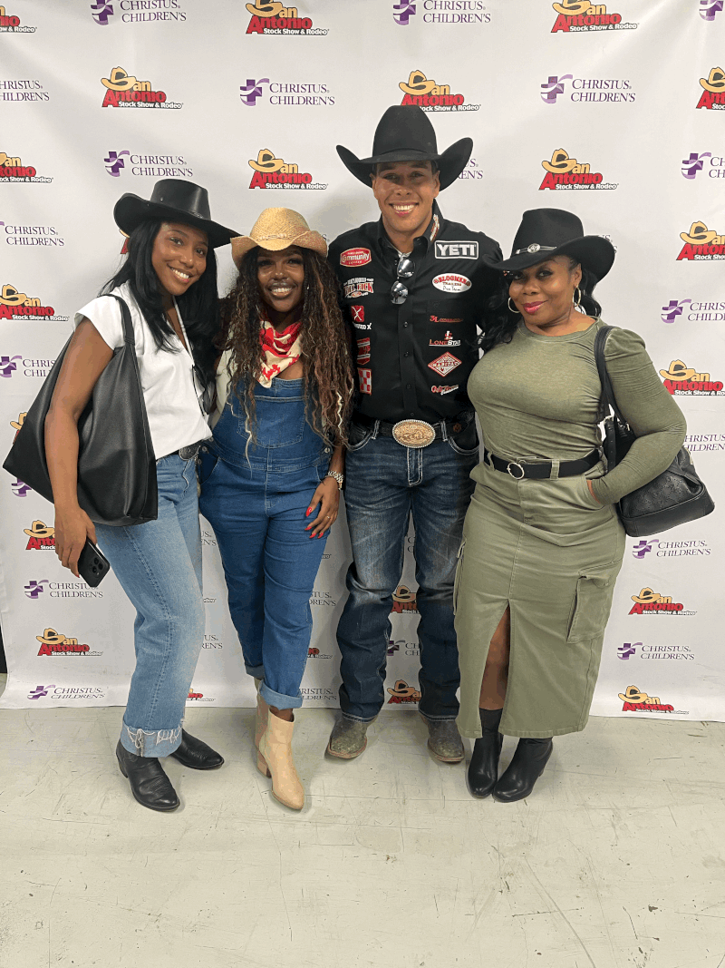 Four people wearing cowboy hats and casual clothing, standing together in front of a backdrop with logos.