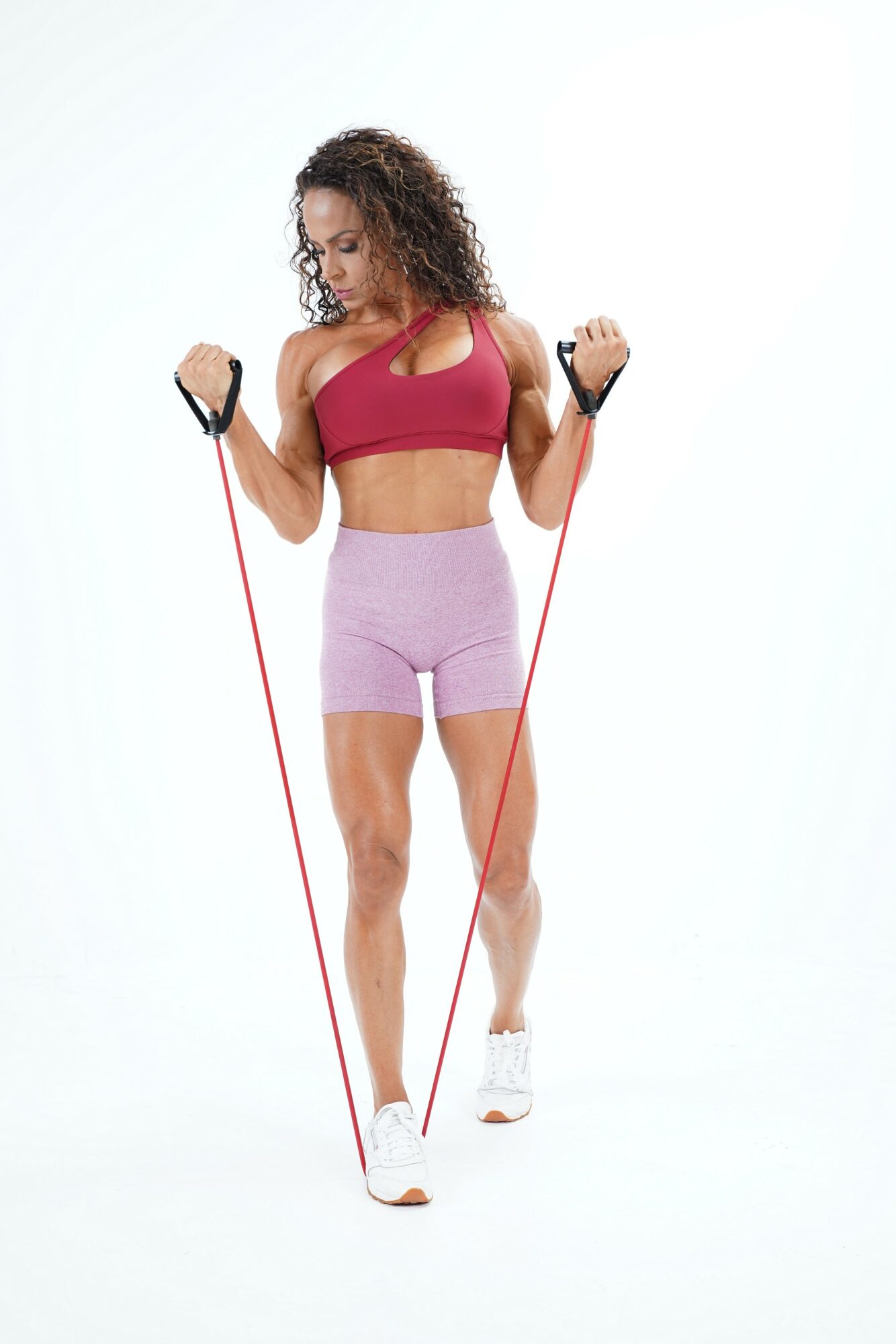 Woman in workout clothes holding resistance bands, standing against a white background.