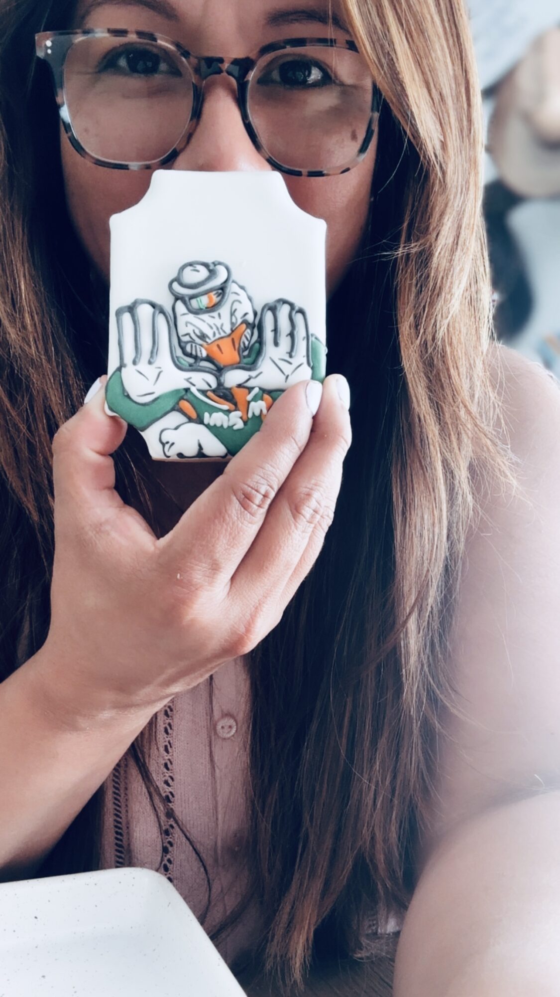 Person with glasses holding a cartoon sticker in front of their face, showing only eyes and part of hair, with a blurred background.