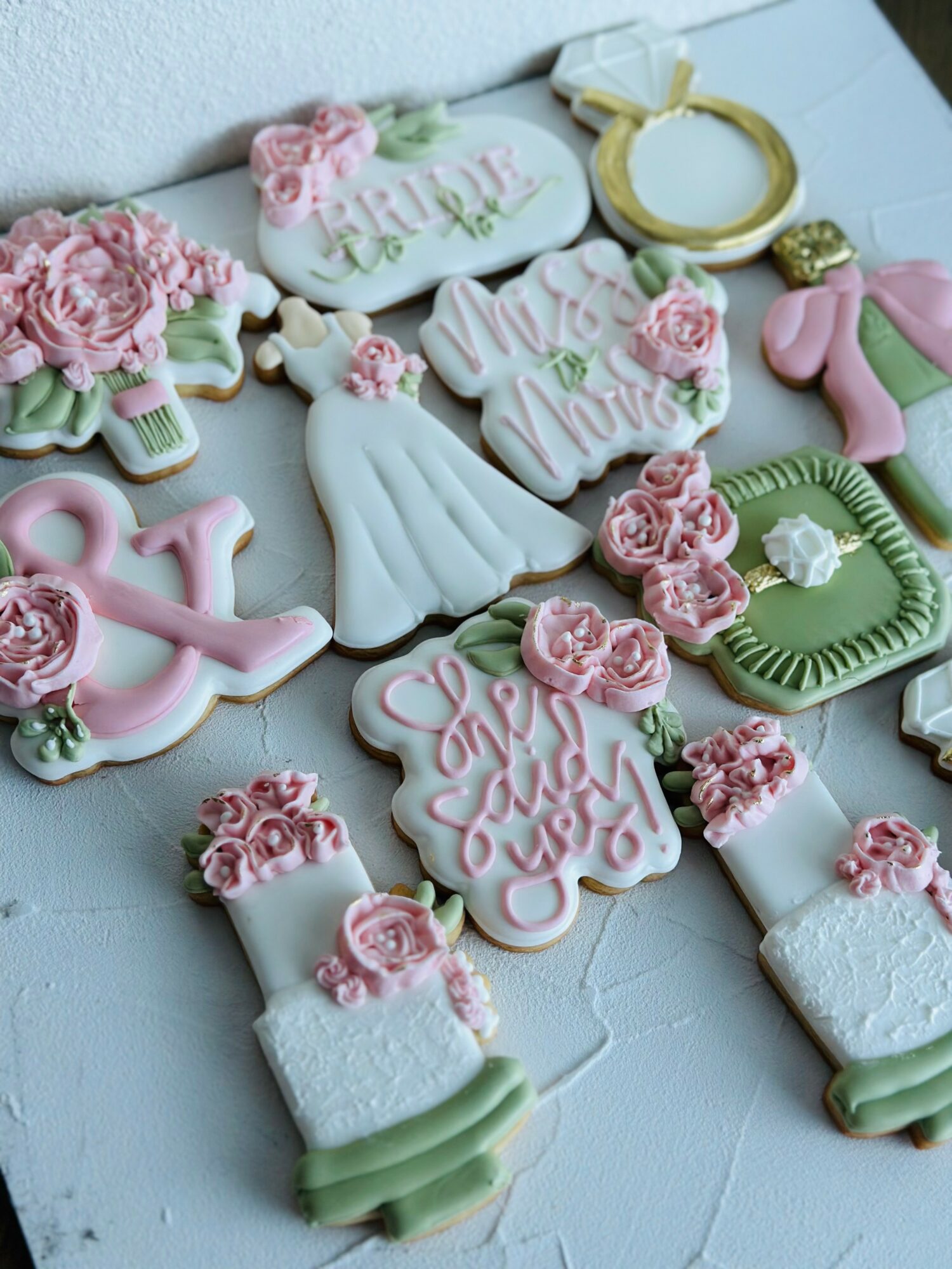 Decorative cookies with pink and green flowers, ribbons, and dresses arranged on a white surface.