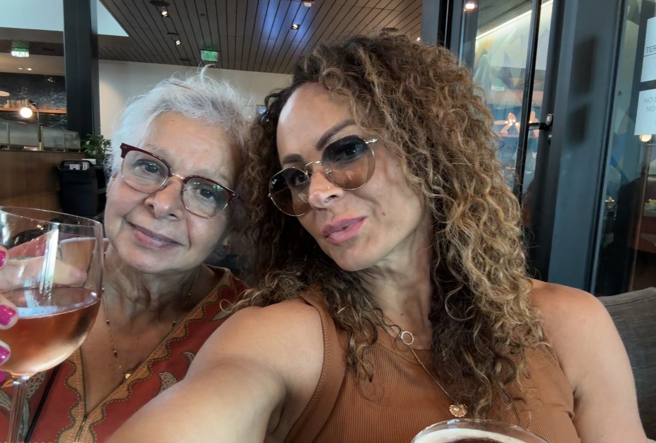 Two women sitting at a table, one holding a glass of wine, smiling at the camera in a restaurant.