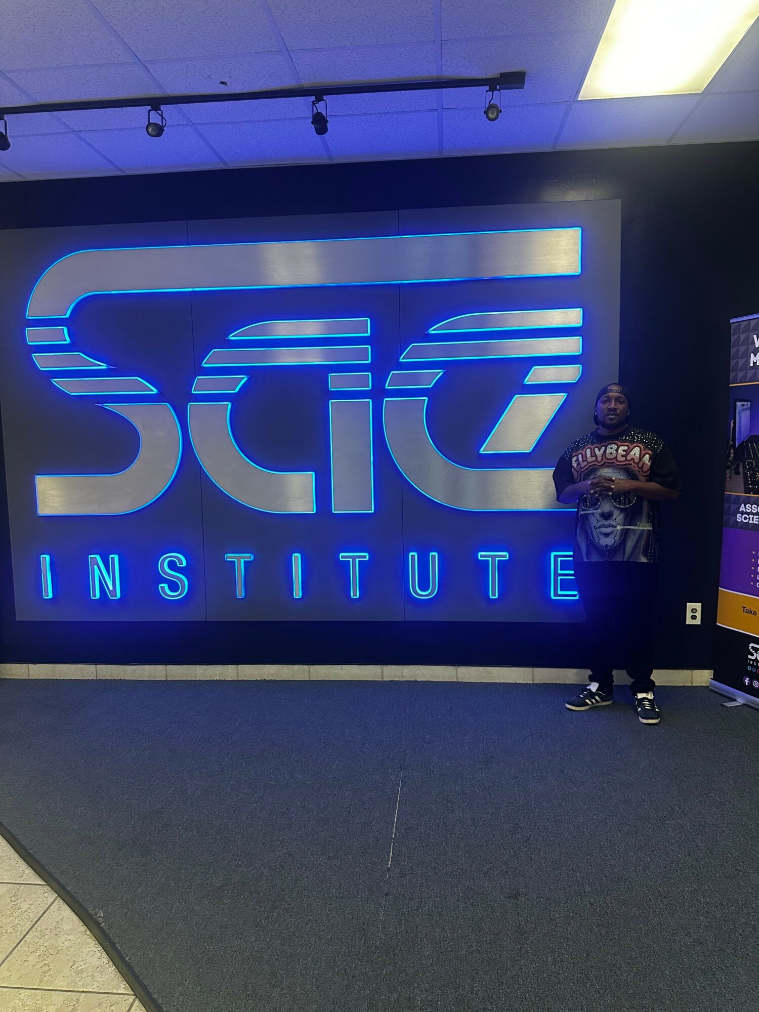 Person sitting on the floor in front of a large illuminated sign reading 'SCC INSTITUTE'.
