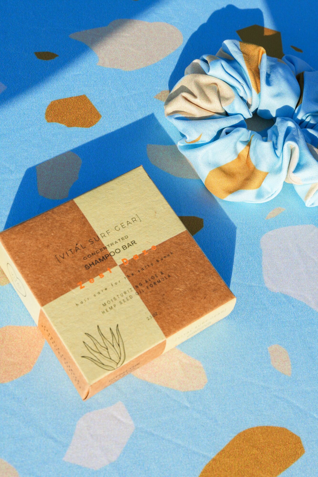 Book with orange and beige cover, and a blue and beige scrunchie on a colorful abstract background.