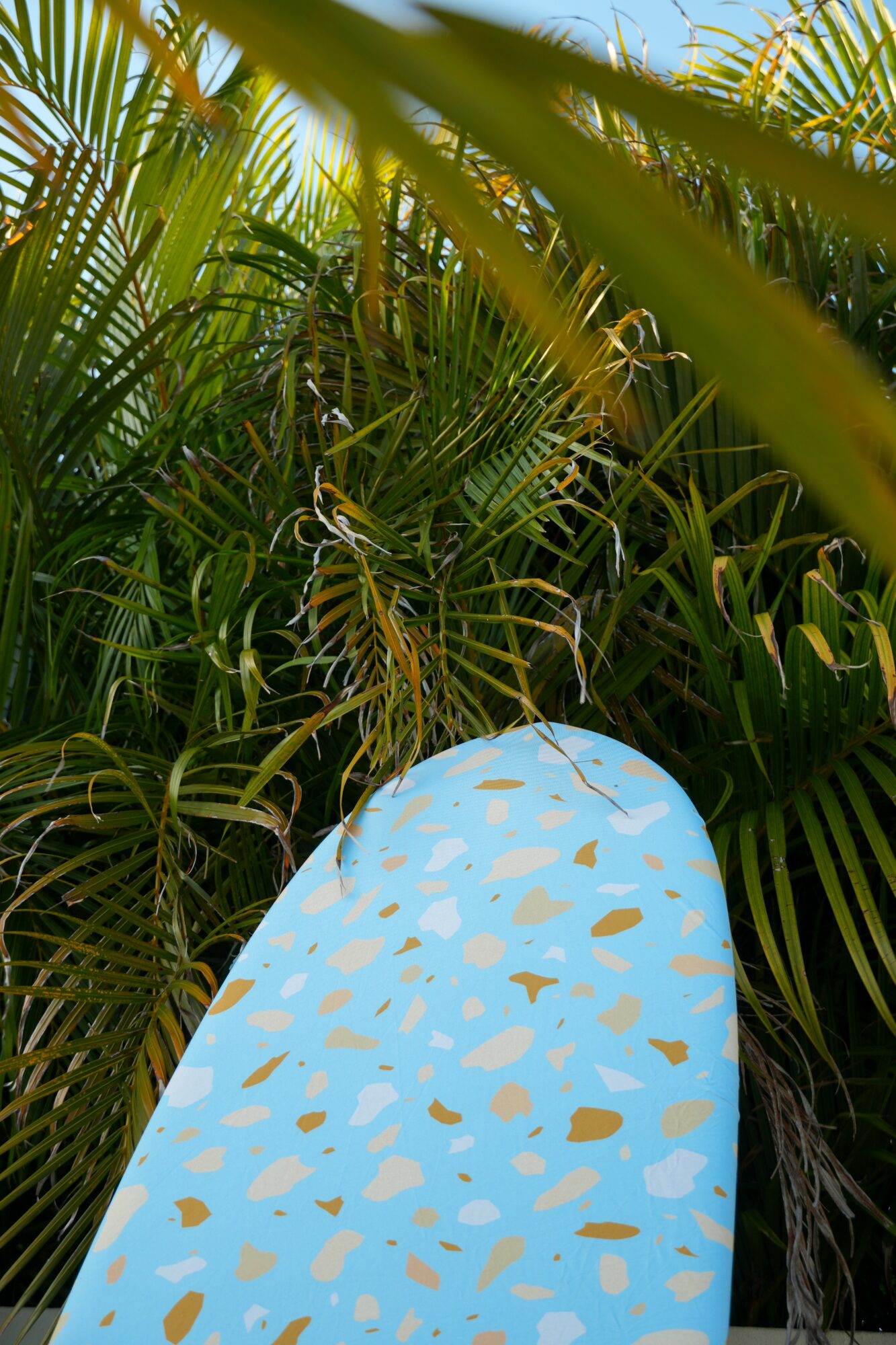 Surfboard with blue and gold pattern leaning among dense green tropical plants.