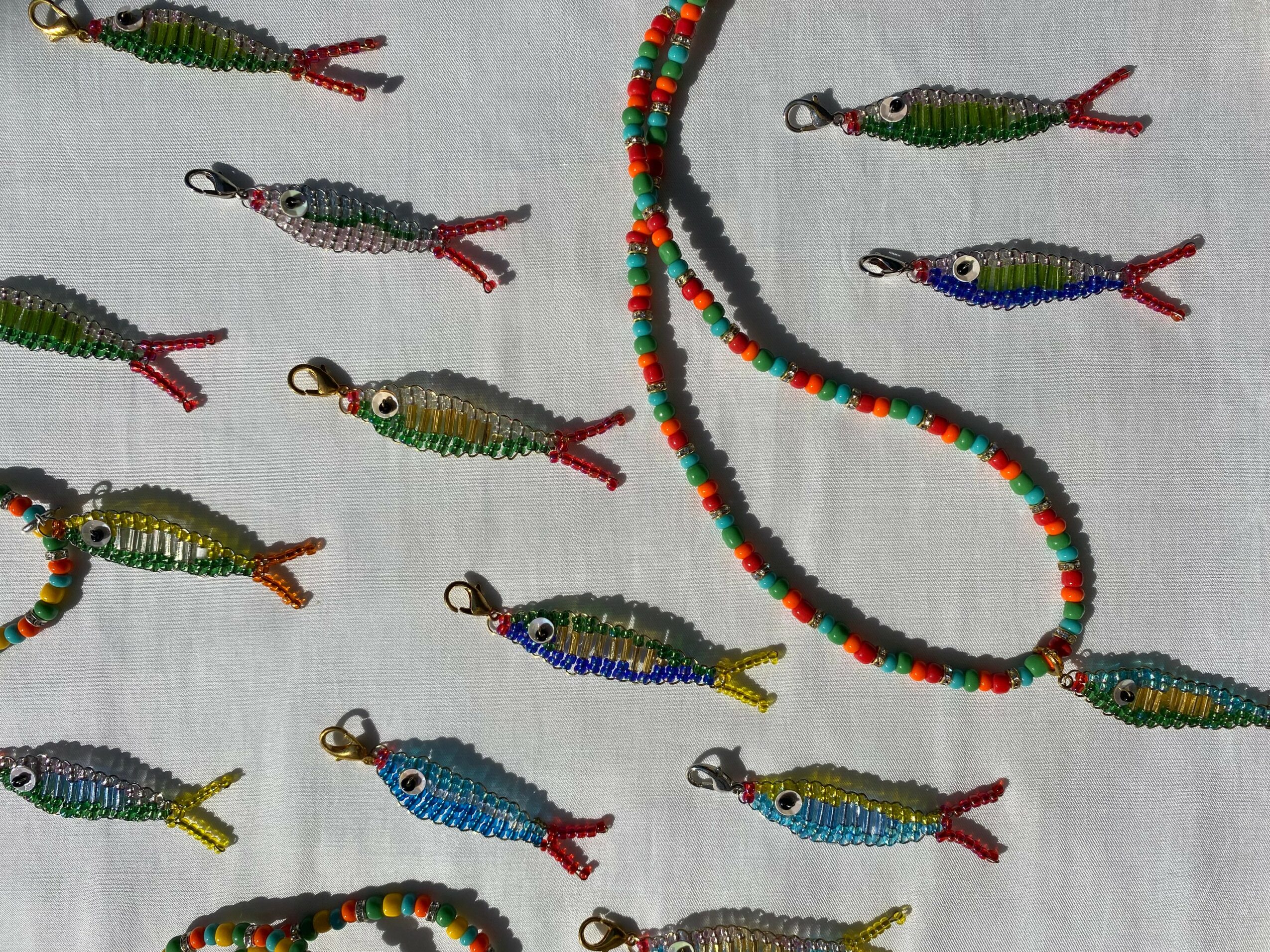 Colorful beaded fish-shaped charms and a beaded necklace on a white surface.