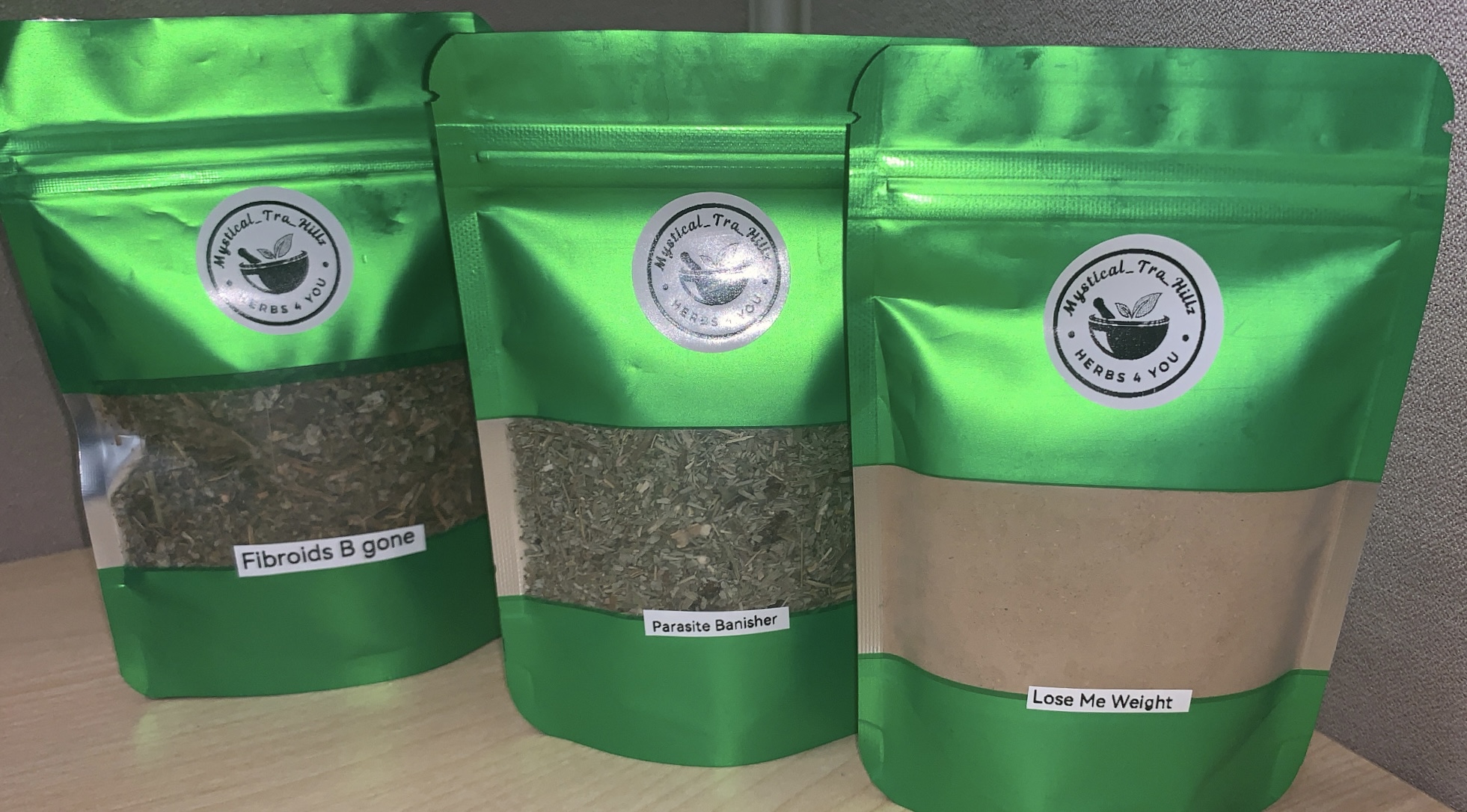 Three green resealable bags with labels, containing different types of herbal products, on a wooden surface.