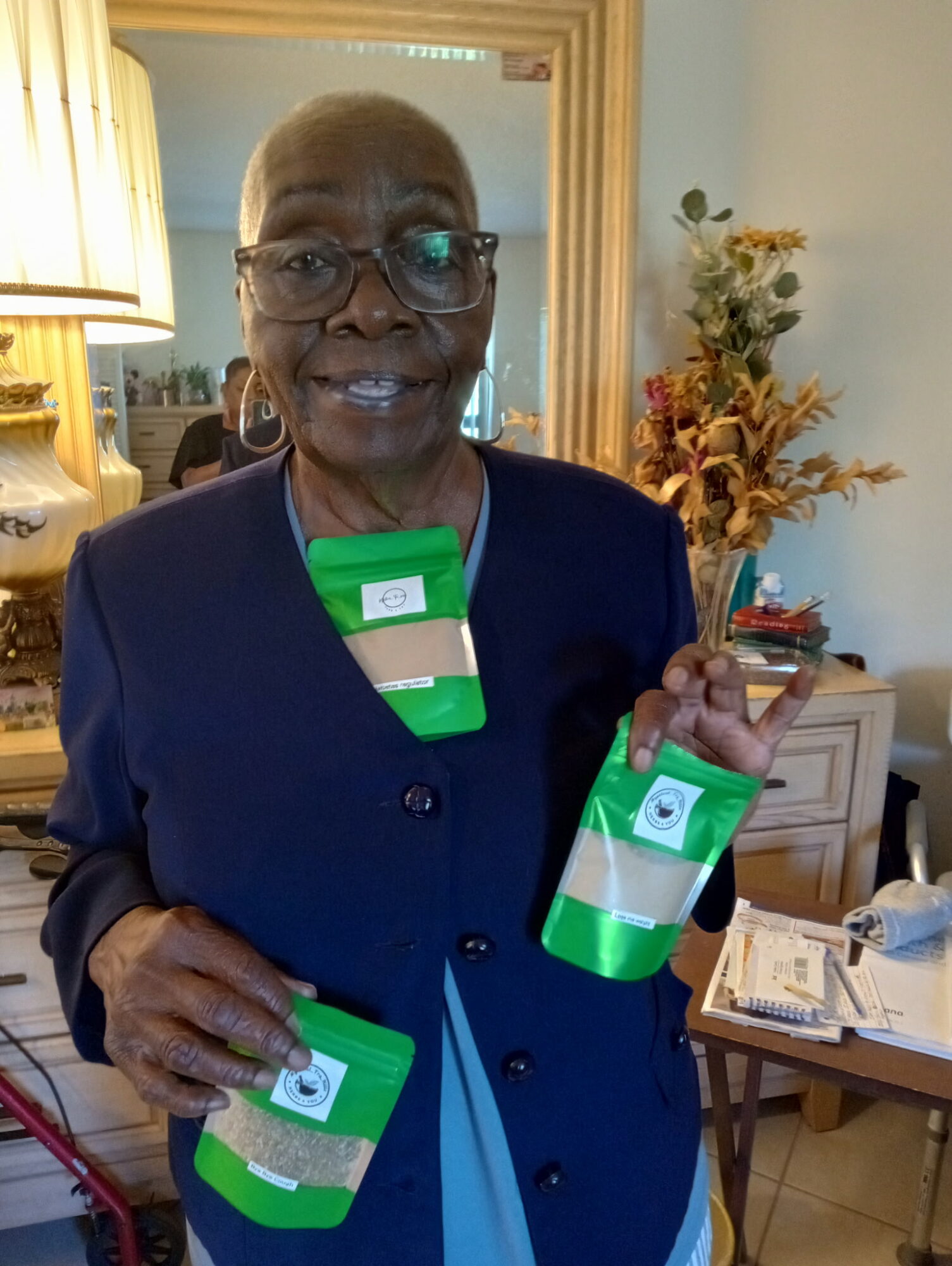 Elderly woman with glasses holding three green and white cans, standing in a living room with a mirror and flowers.
