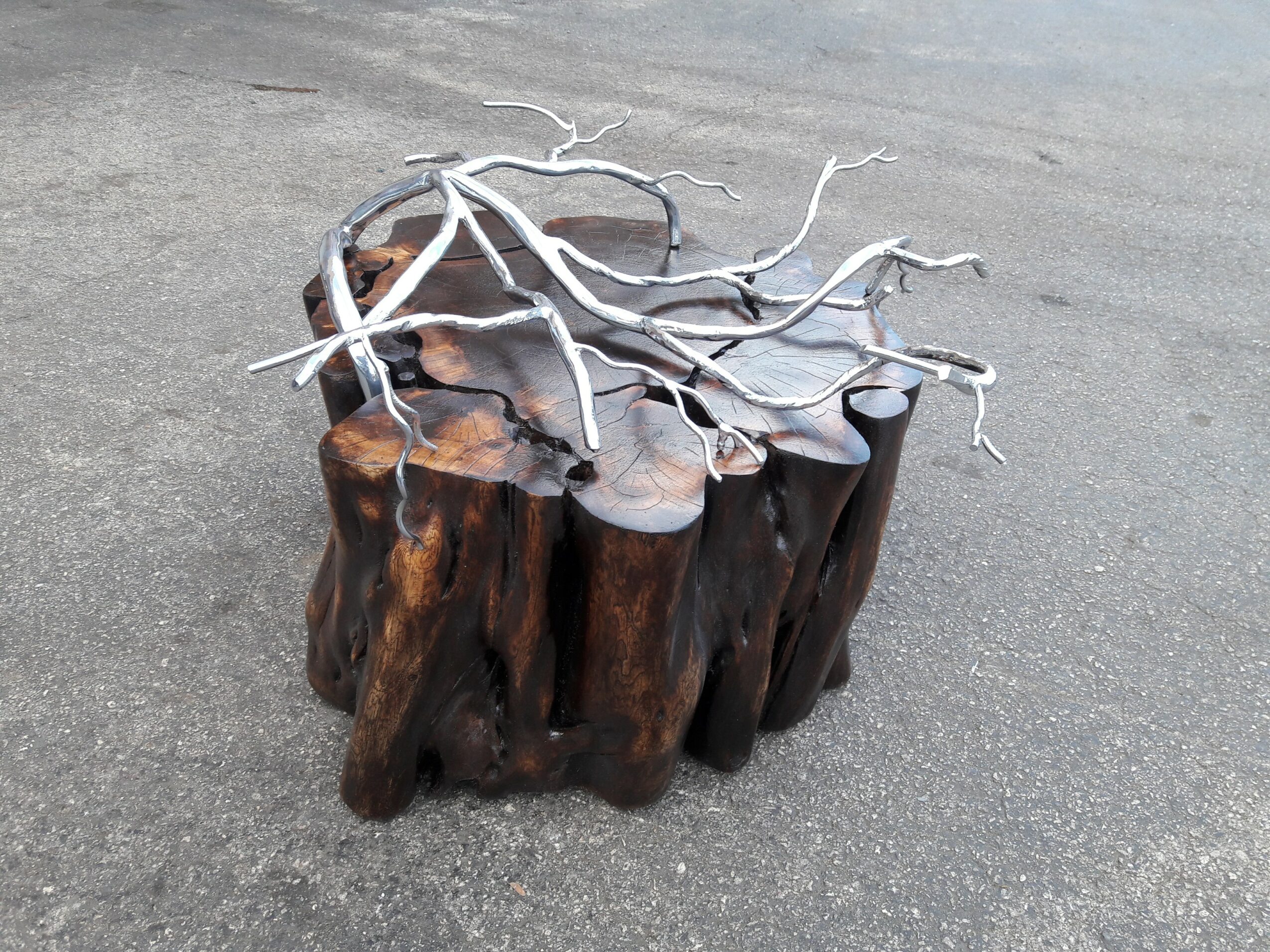 A wooden stump with a metal branch sculpture on top, placed on a paved surface.