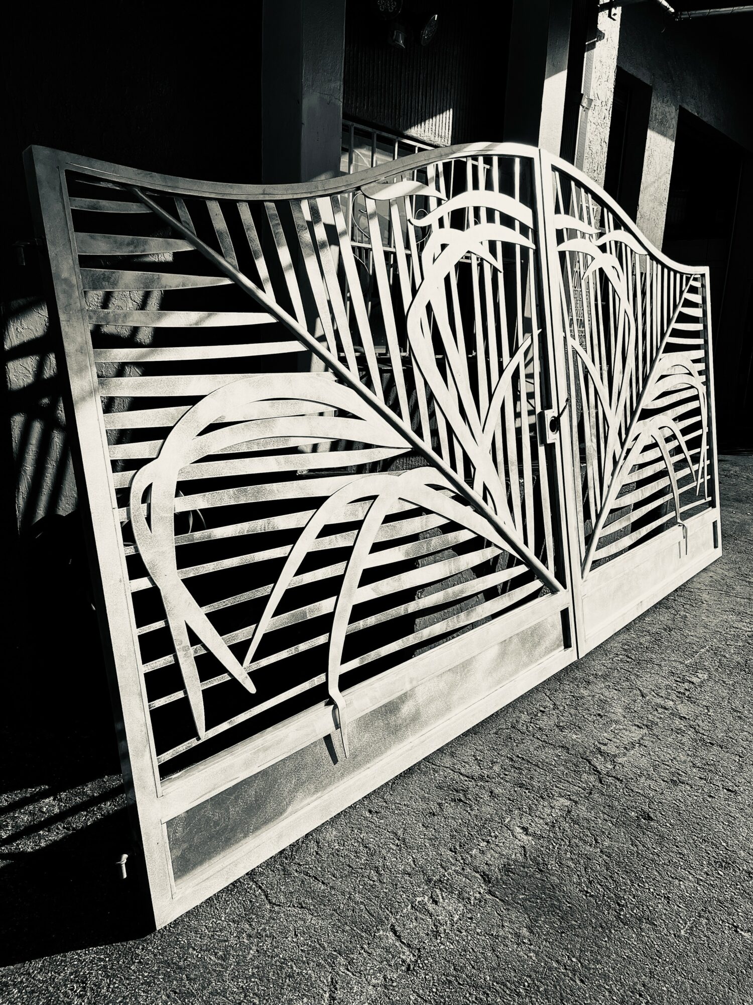 Decorative metal gate with curved and linear patterns, leaning against a dark wall, on a concrete floor.