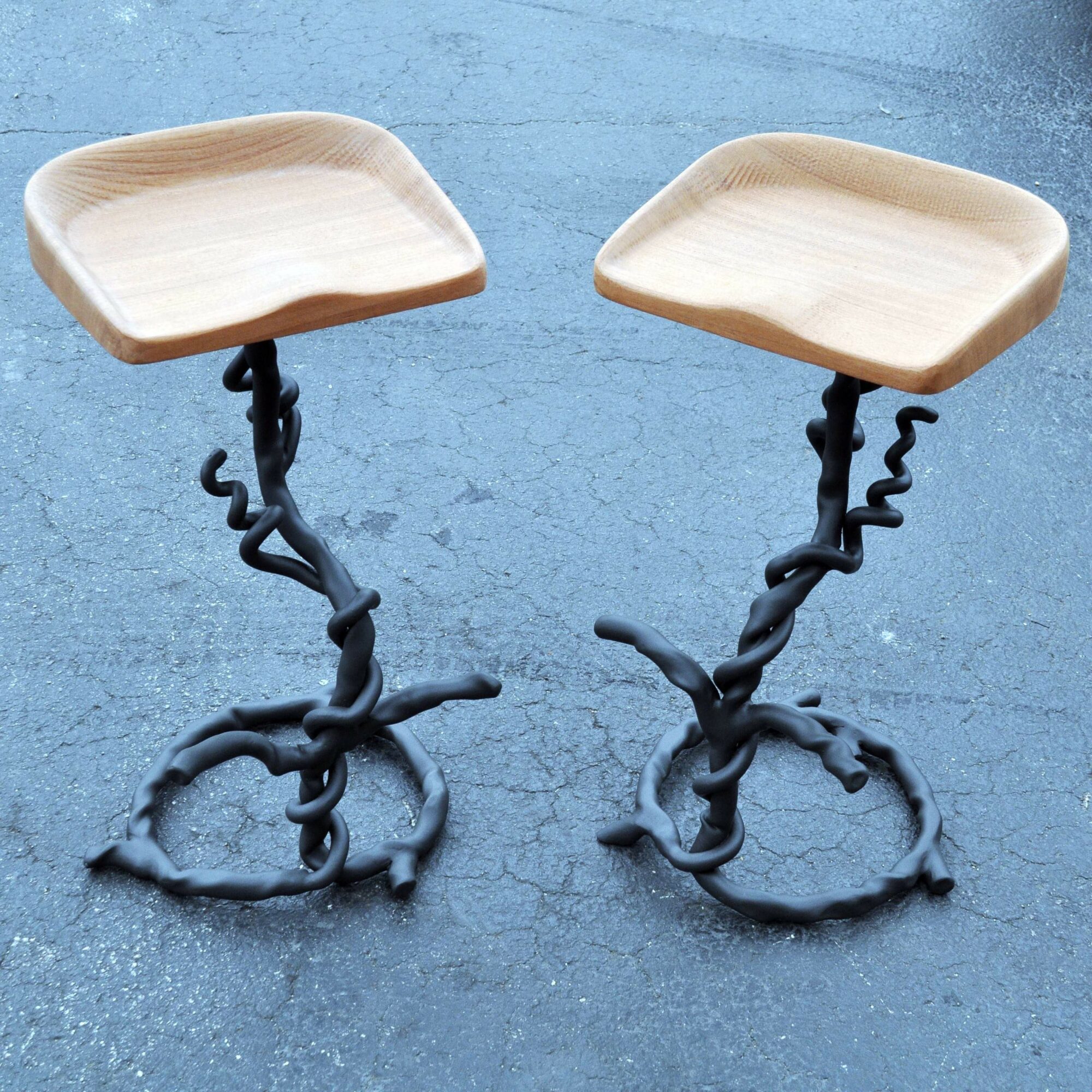 Two stools with twisted metal bases and wooden seats on a textured blue surface.