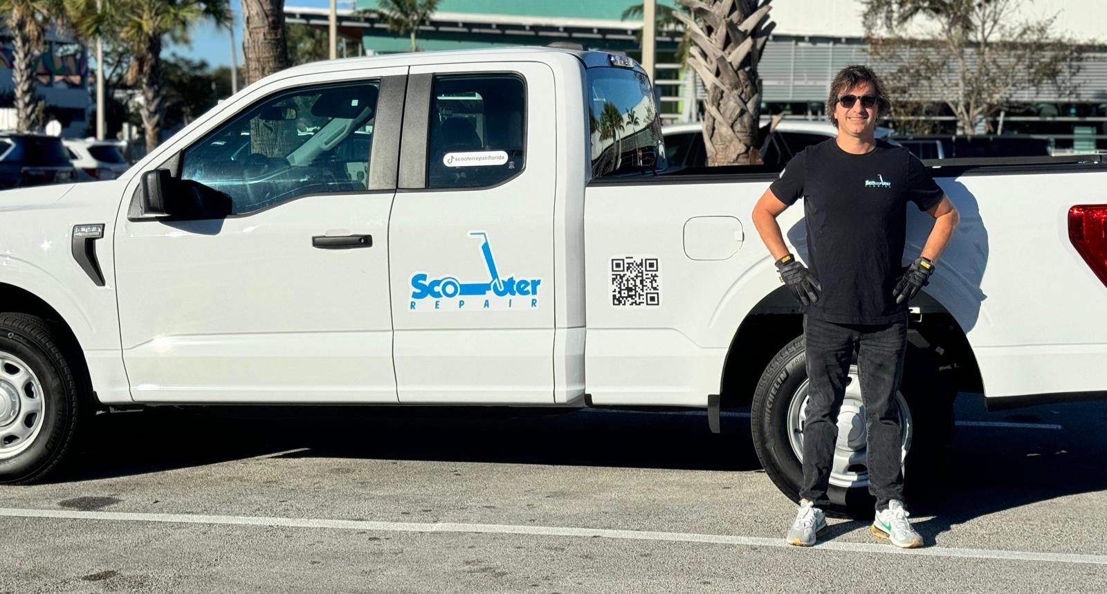 Person standing next to a white pickup truck with a logo and QR code, in a parking lot.