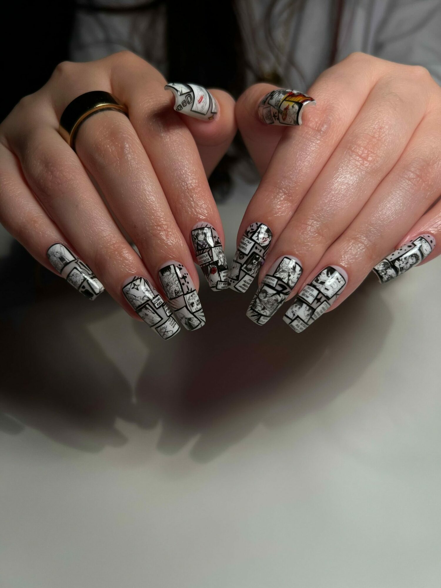 Hands with detailed black and white patterned nail art, rings on fingers, resting on a smooth surface.