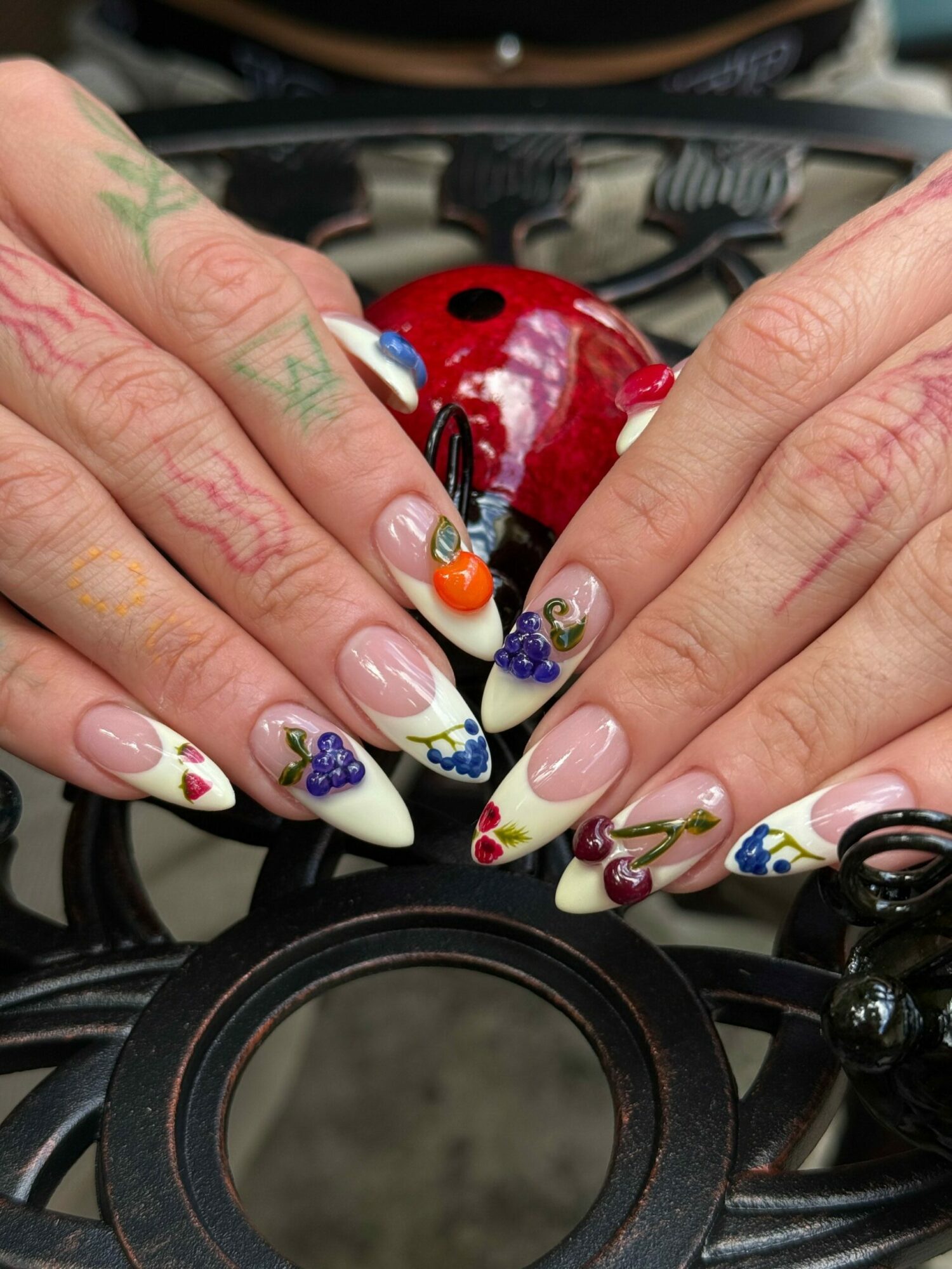 Close-up of hands with decorated nails, holding a camera lens, with colorful floral and ladybug nail art.