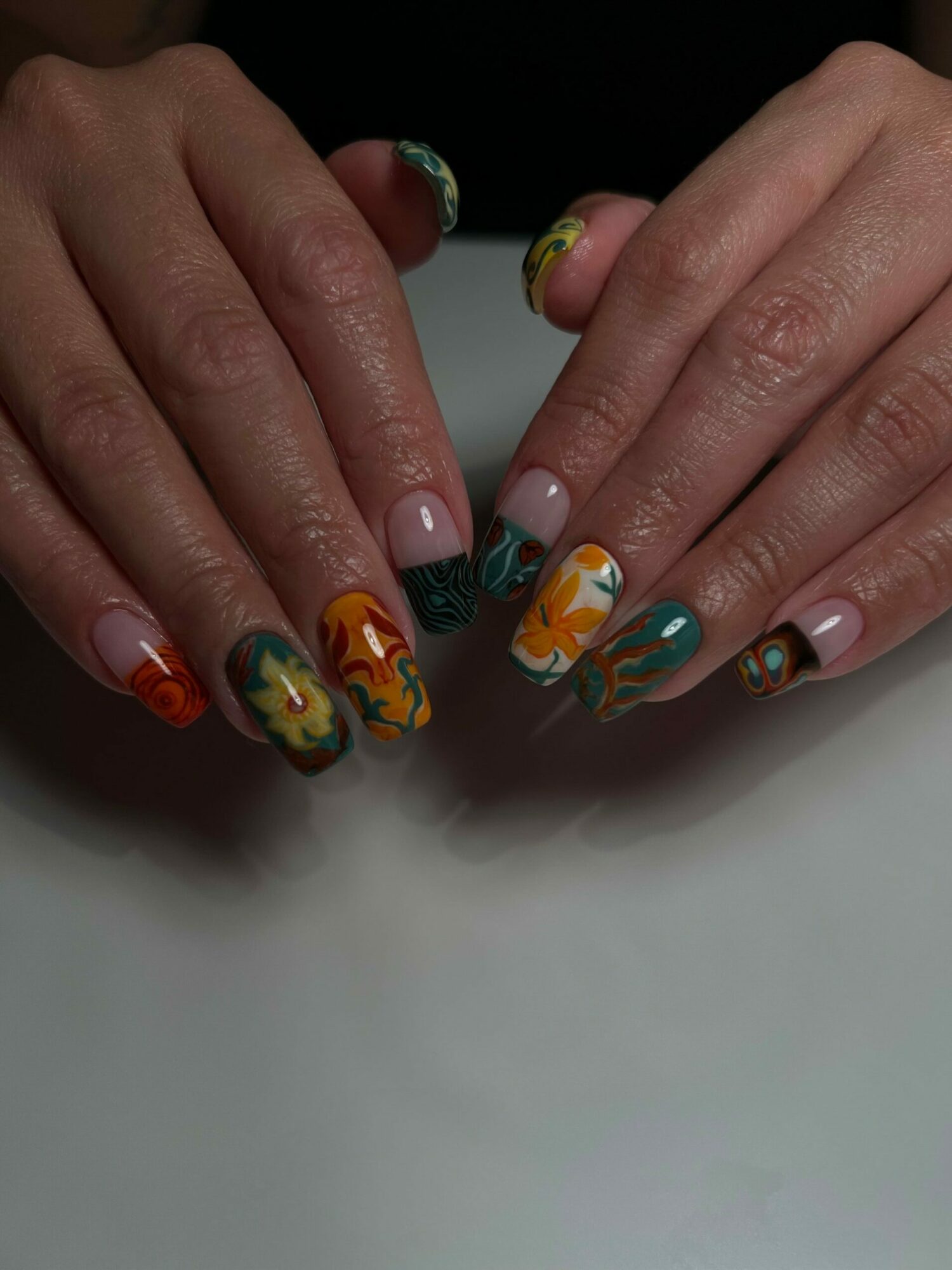 Two hands with colorful, patterned nail art, resting on a white surface.