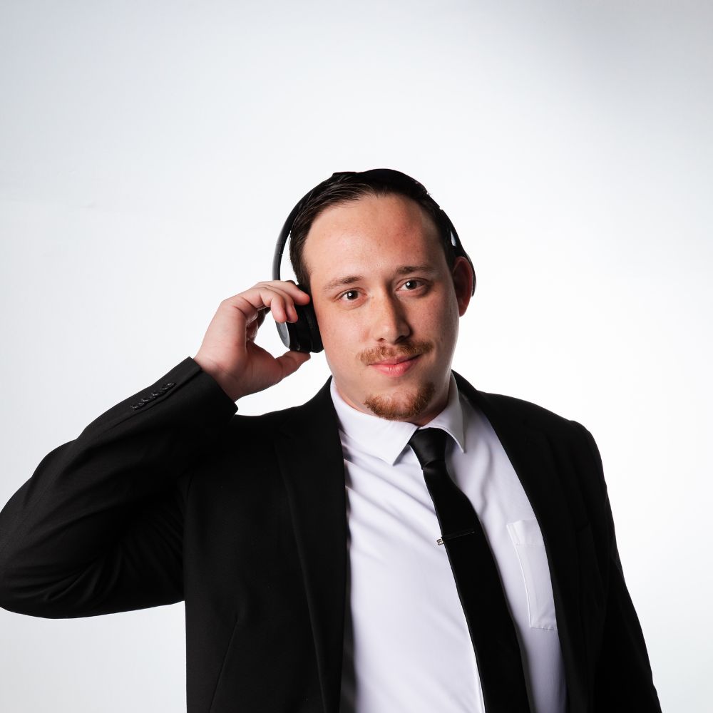 Man in suit wearing headphones, adjusting them with his right hand, smiling slightly, against a plain white background.