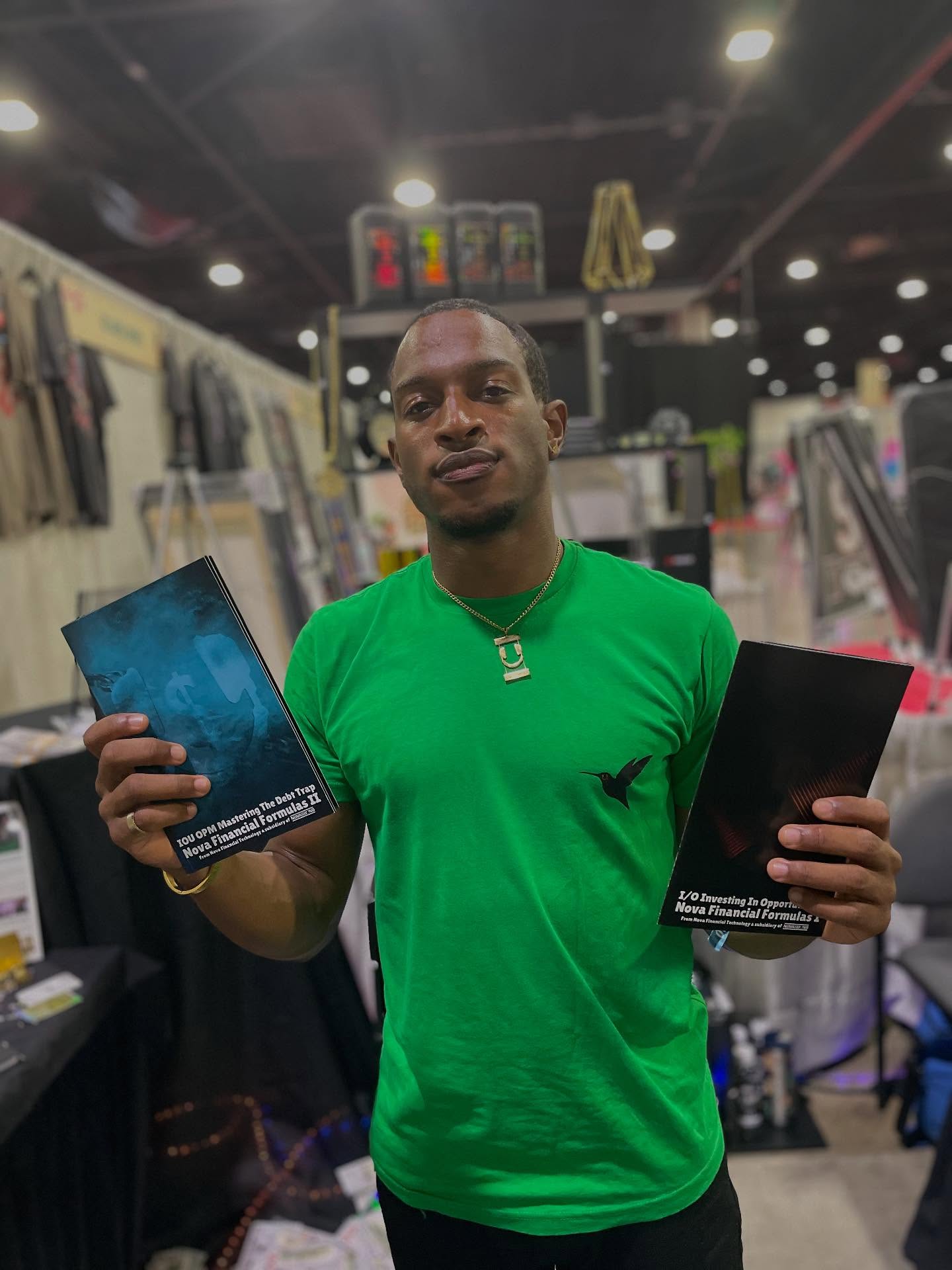 Man in green shirt holding two black boxes in a store, with display items and bright ceiling lights behind him.