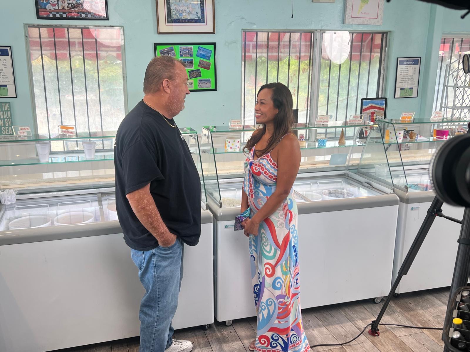 A man and woman are talking inside a store with glass display cases and framed pictures on the wall.