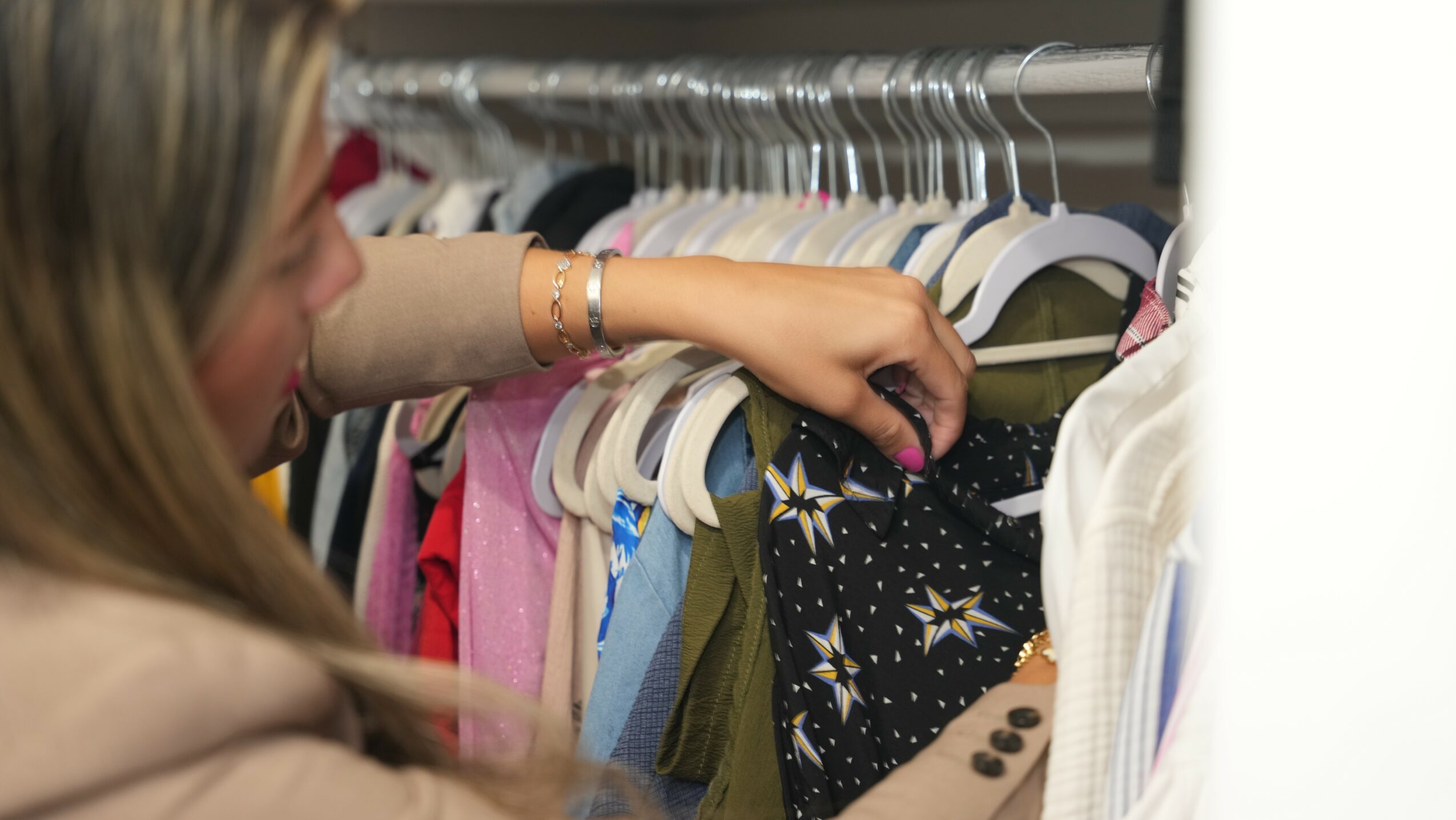 Person browsing clothes in a closet, selecting a garment from a hanging rack.