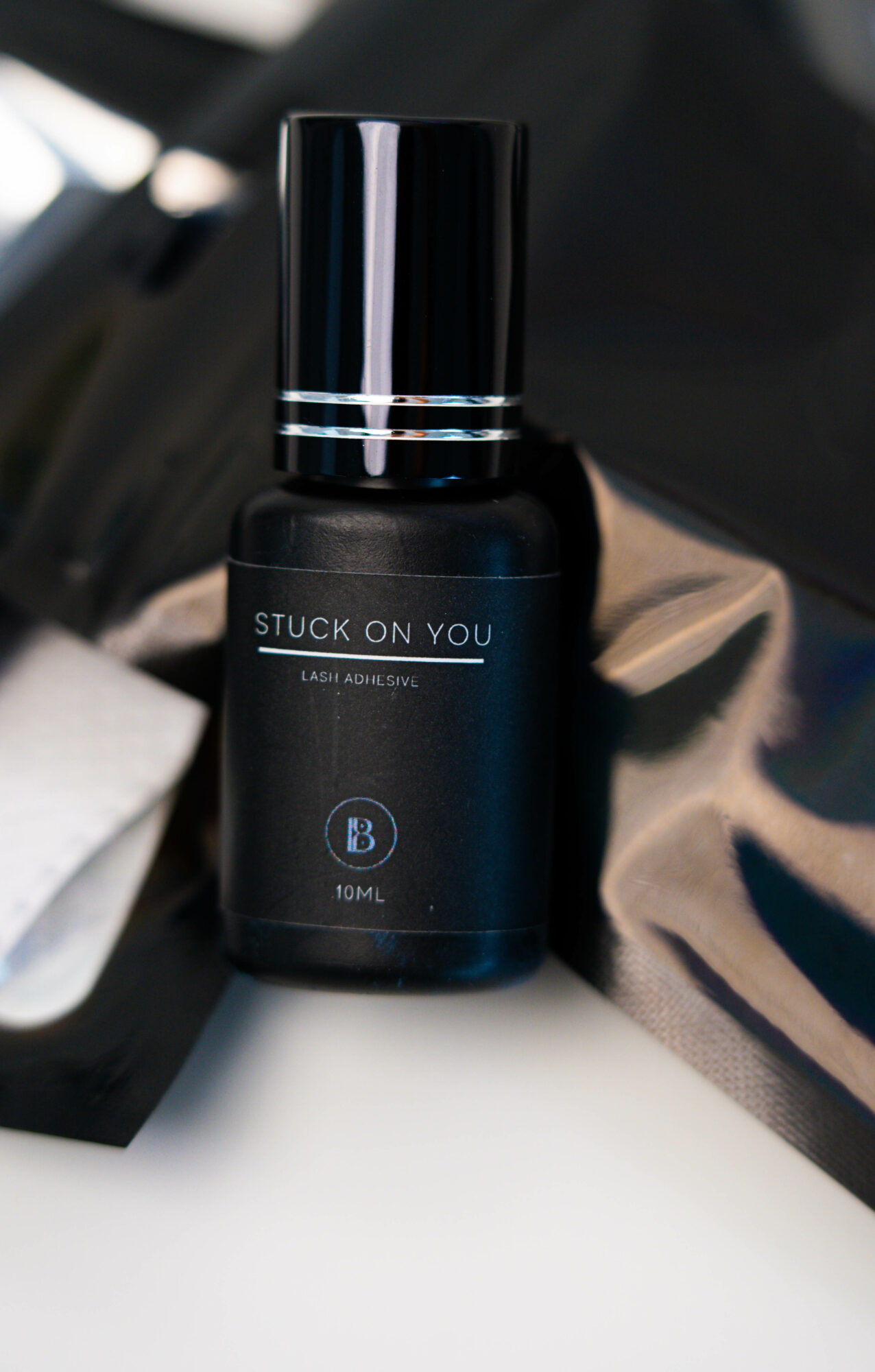 Black bottle with a shiny black cap, labeled 'STUCK ON YOU' and 'B' logo, on a reflective surface.