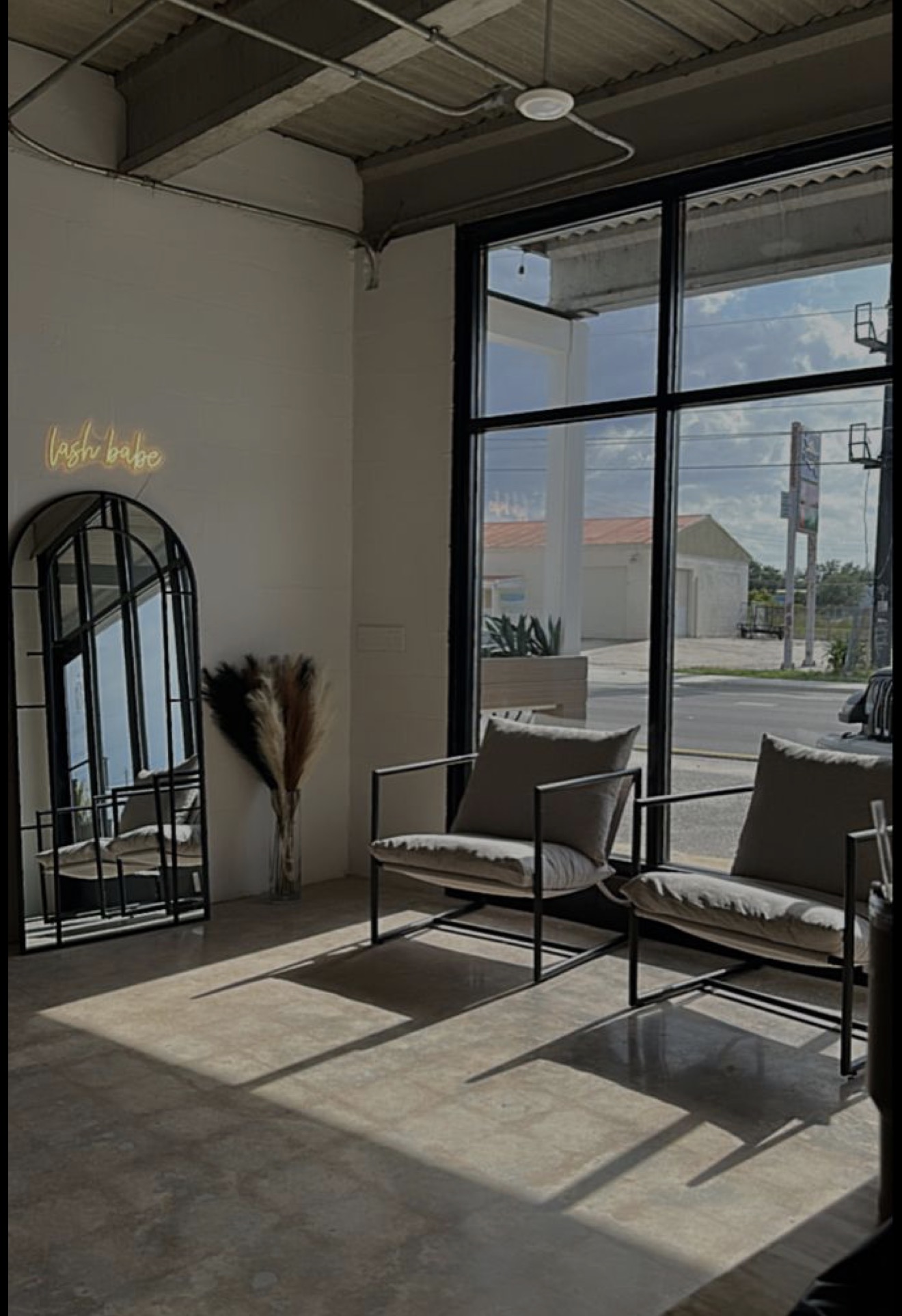 Interior with two chairs, a mirror, and a window showing an outdoor scene, sunlight casting shadows on the floor.