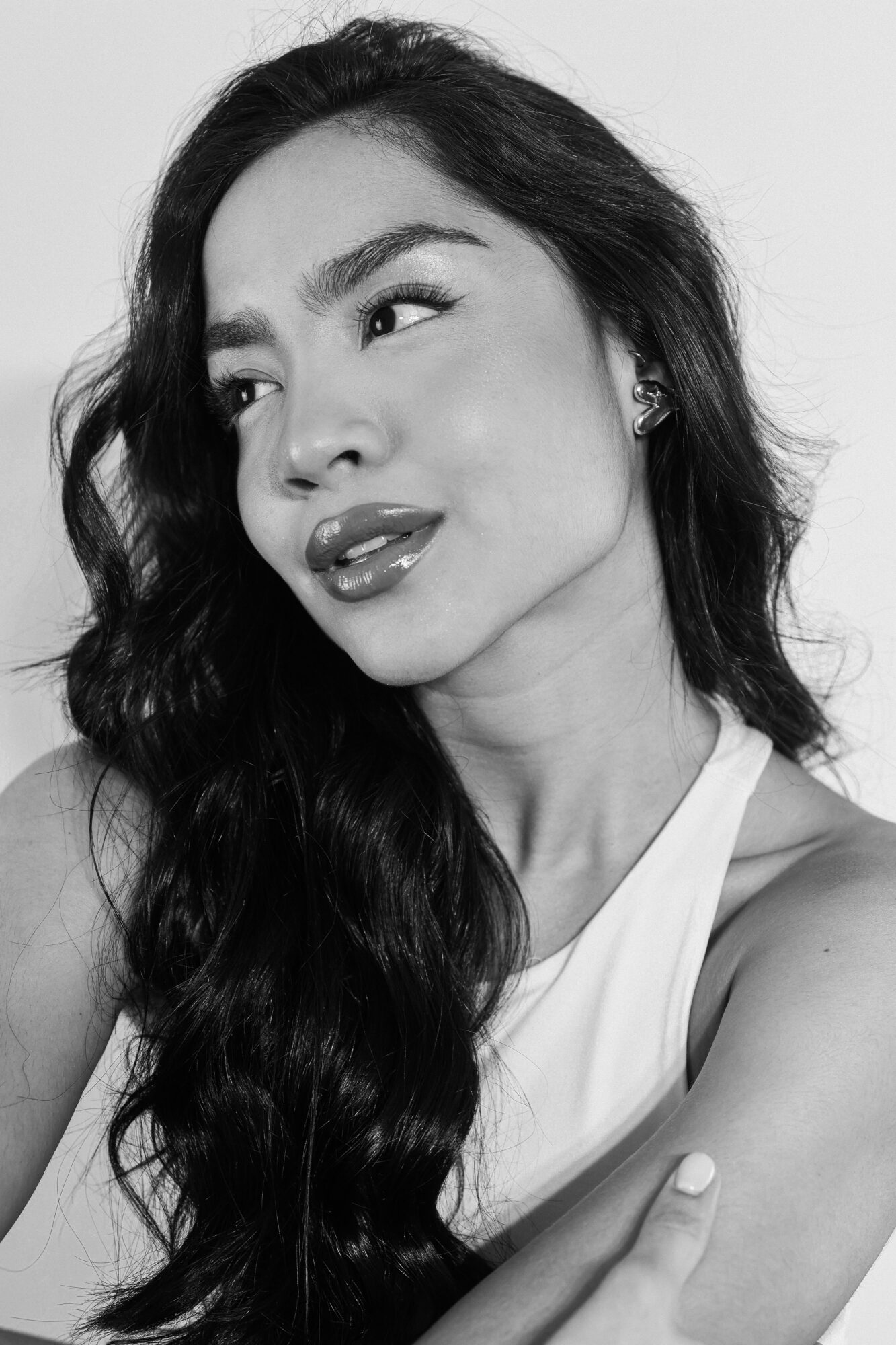 Woman with long wavy hair looking to the side, wearing a sleeveless top, in black and white.