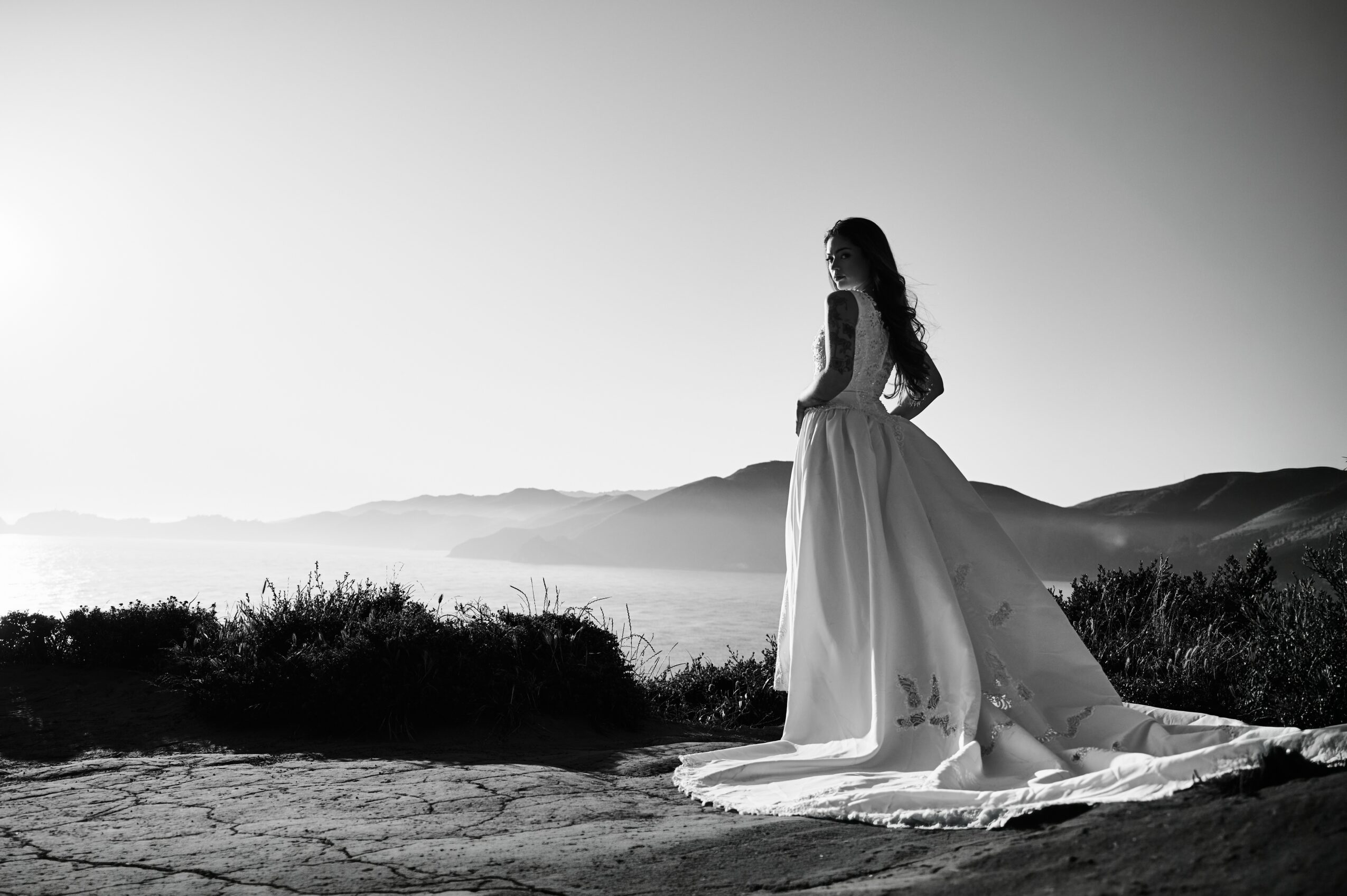 Woman in a long dress standing on a landscape with mountains in the background, black and white image.