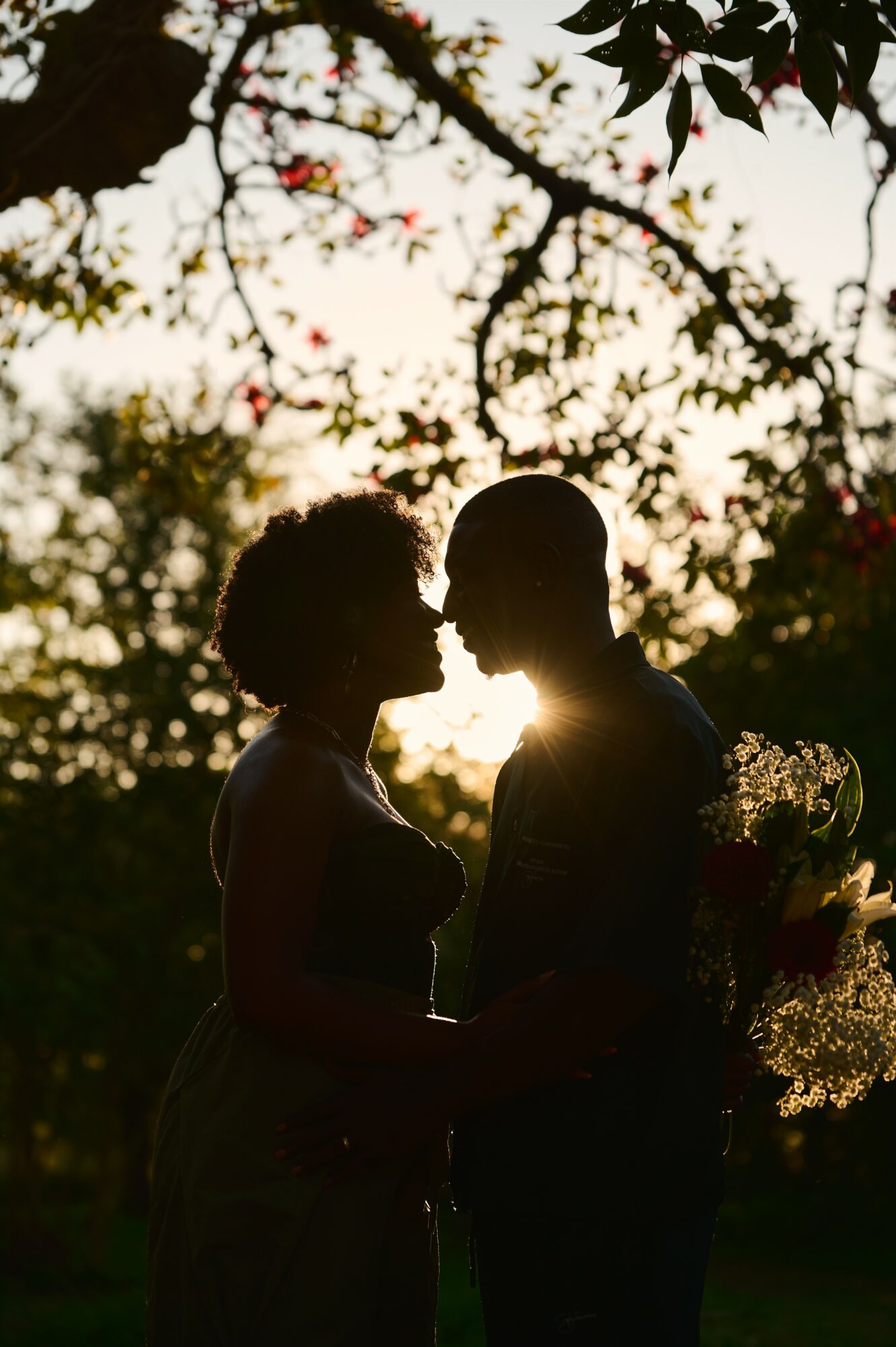 Silhouettes of a couple facing each other outdoors with trees and sky in the background.