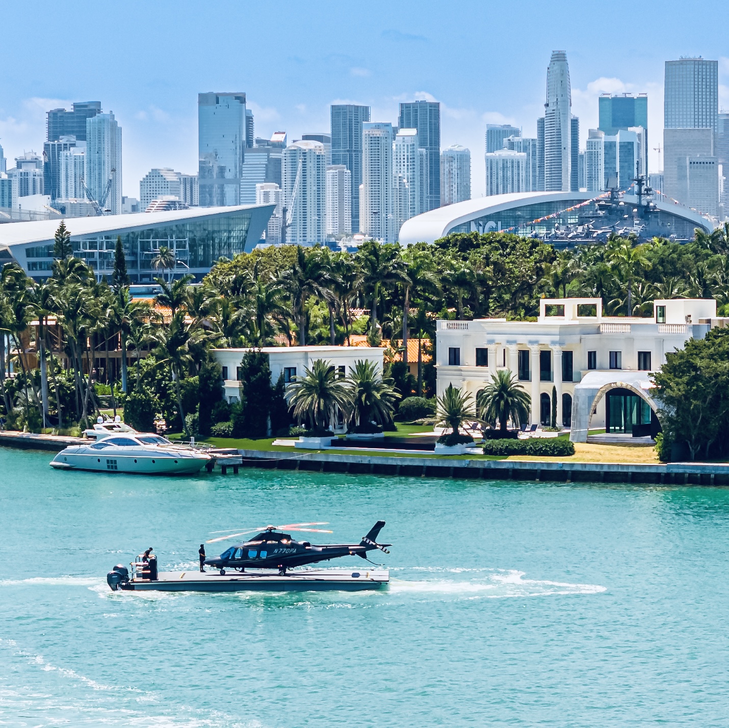 City skyline with tall buildings, a waterfront with boats, and lush greenery in the foreground.