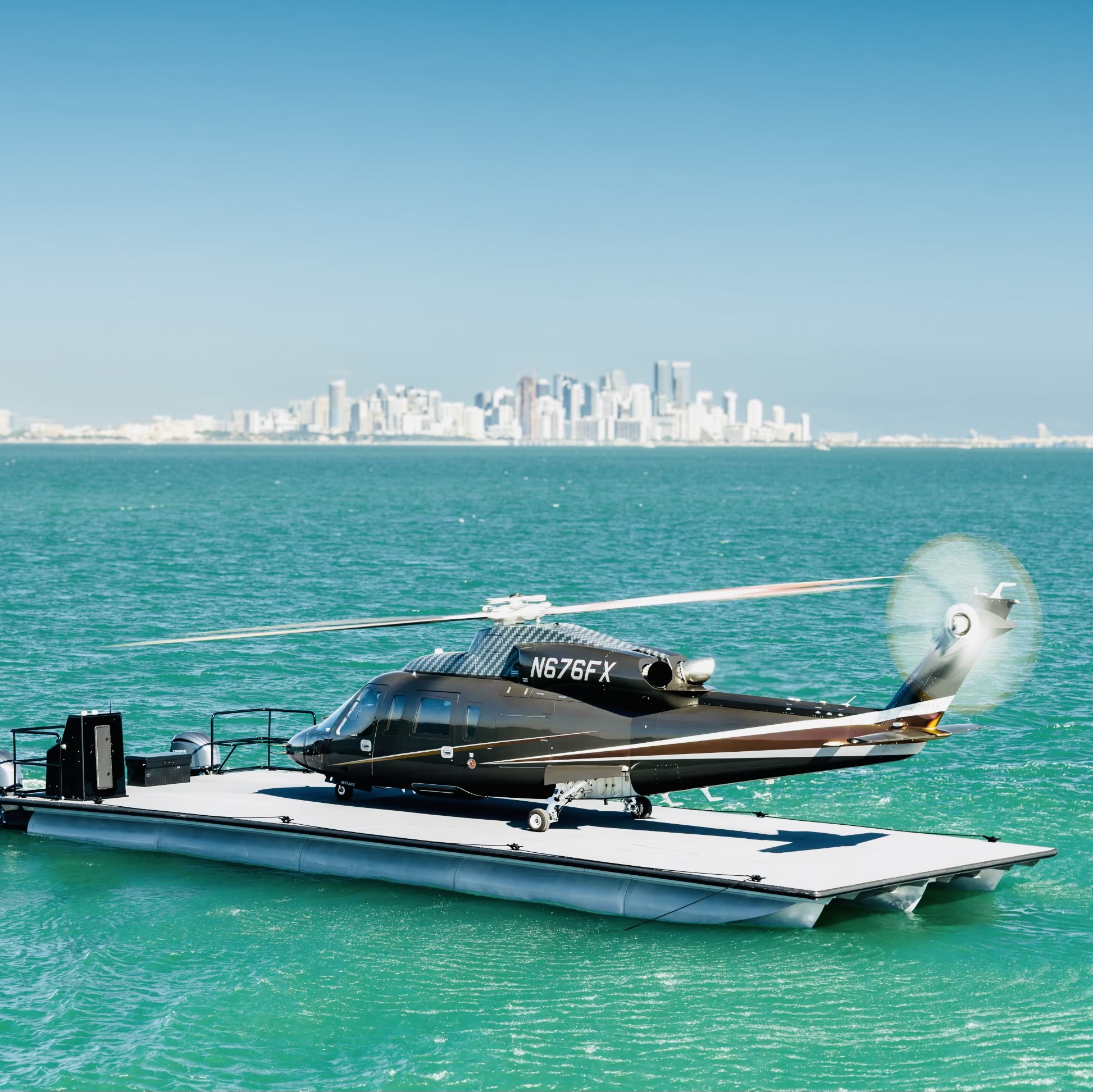 Helicopter on a floating platform over turquoise water with city skyline in background.