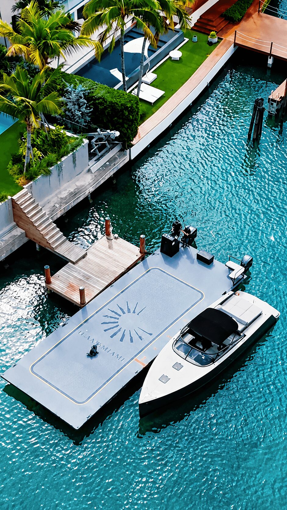 A boat docked at a floating platform with a pool, surrounded by water, greenery, and a deck area with stairs.