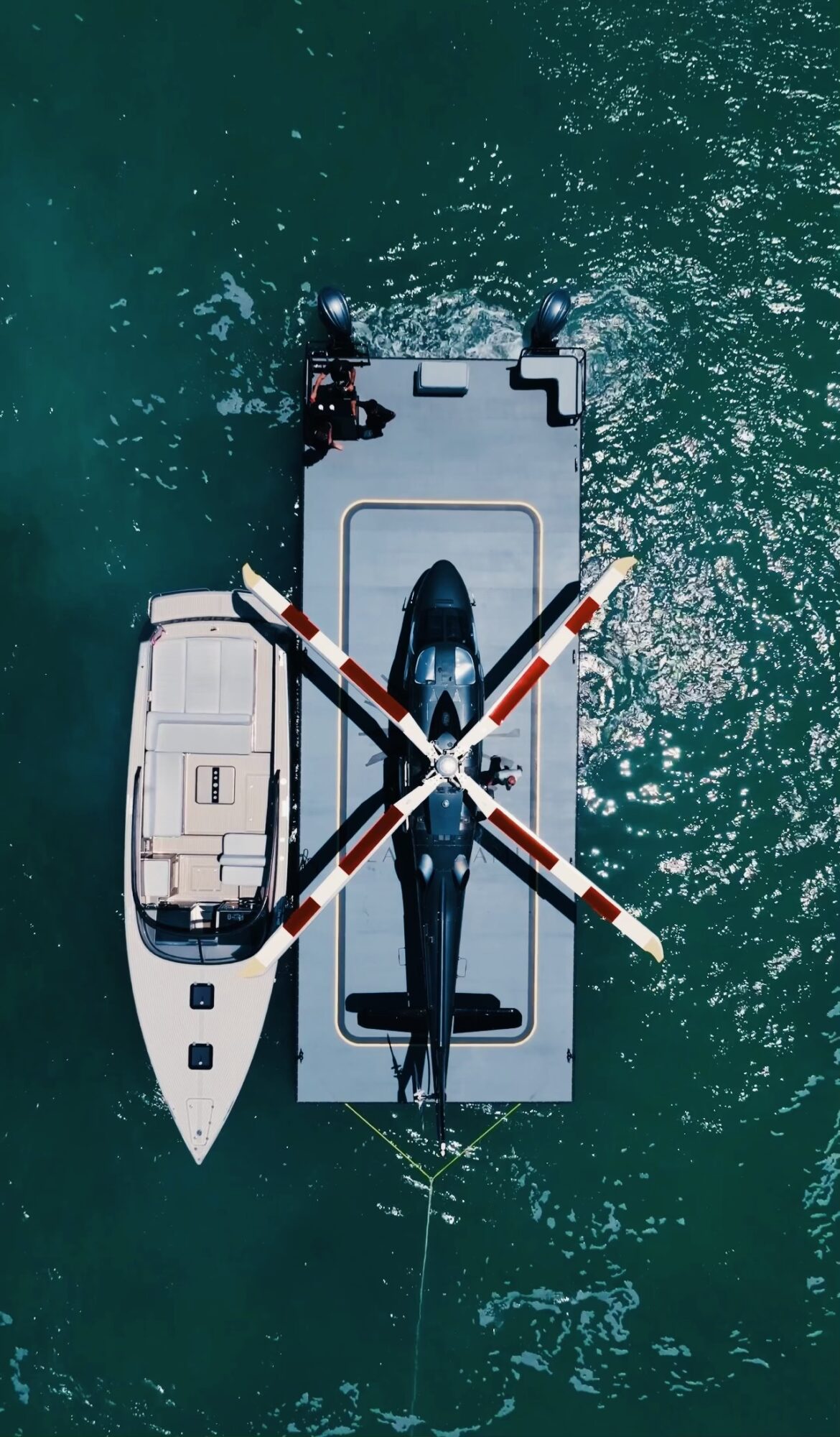 A helicopter is on a boat, viewed from above, with water surrounding it.