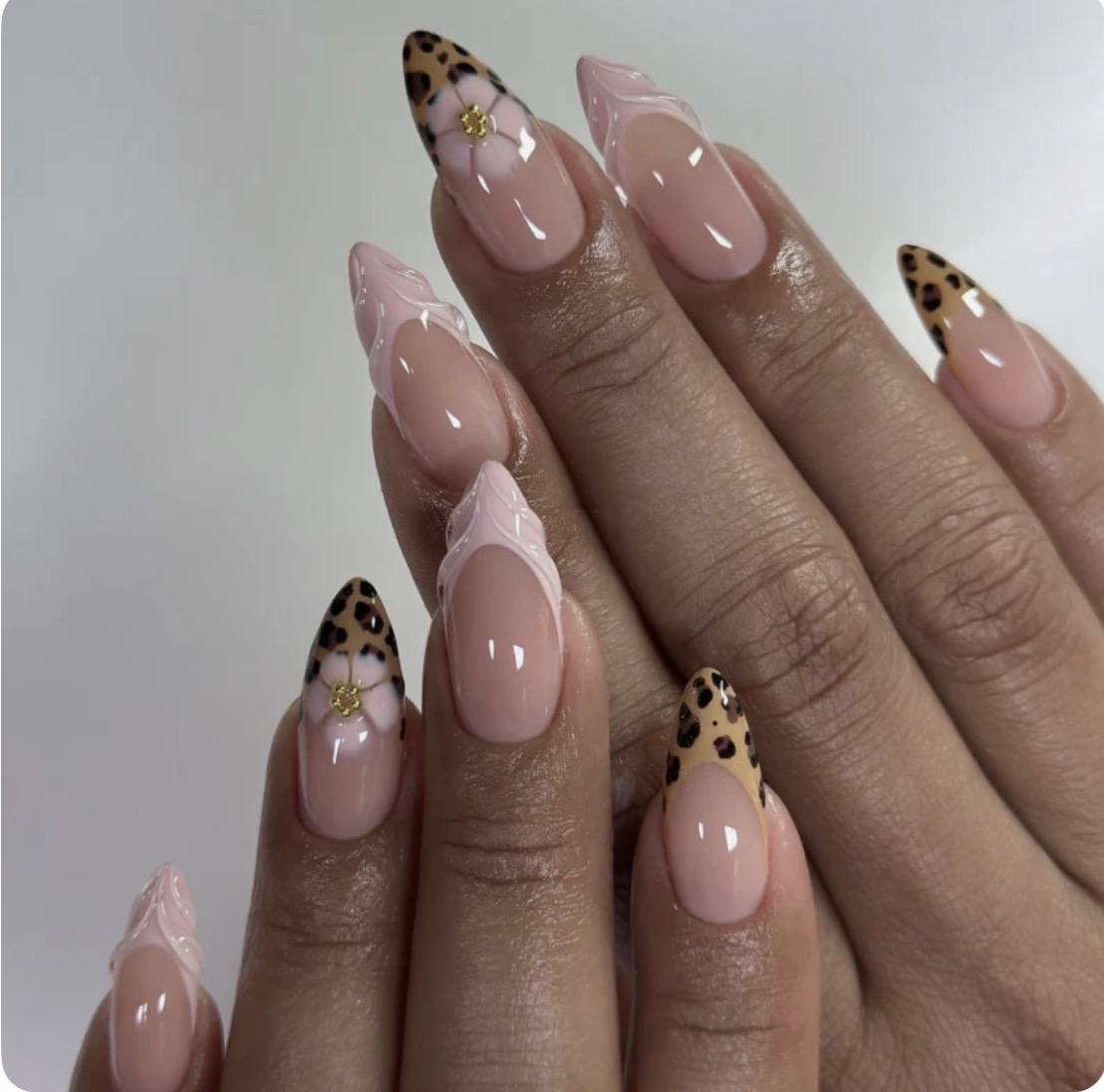 Close-up of hands with manicured nails featuring pink polish and leopard print tips, decorated with small gold accents.