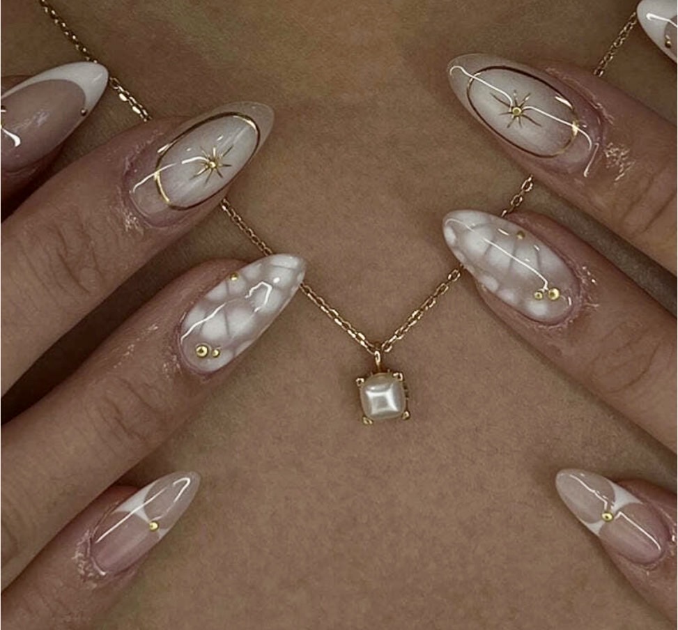 Person wearing a gold necklace with a square pendant, and long, decorated nails with white and gold designs.