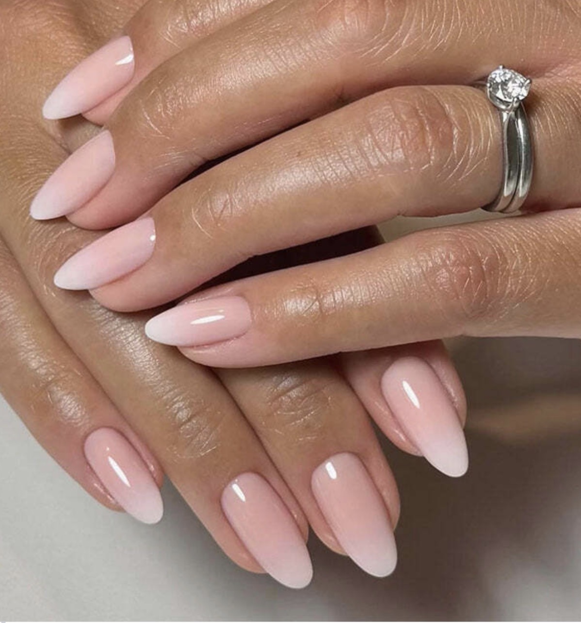Close-up of hands with manicured nails and a ring with a large gemstone, showing well-groomed skin and polished nails.