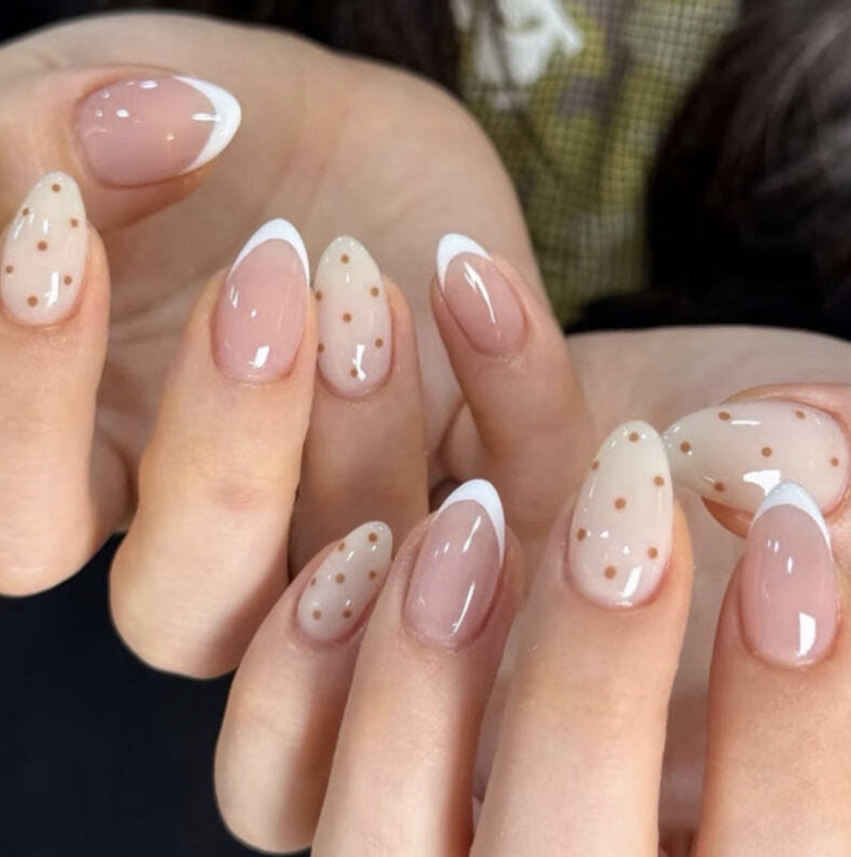 Close-up of hands with manicured nails, some with white tips and polka dots, others with clear polish, in natural light.