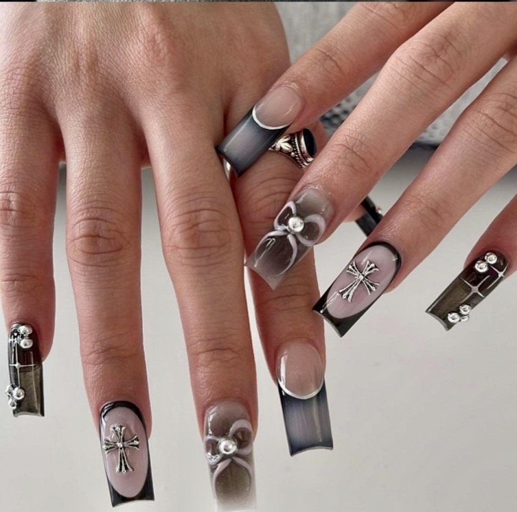 Hands with decorated nails and rings, displaying black, pink, and gray nail art with embellishments.