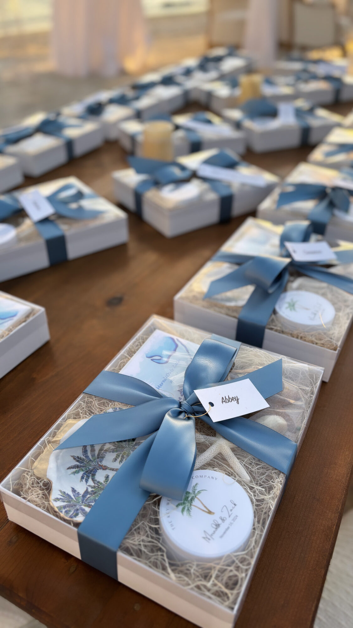 Multiple gift boxes with blue ribbons arranged on a wooden table, some open showing decorated cookies inside.