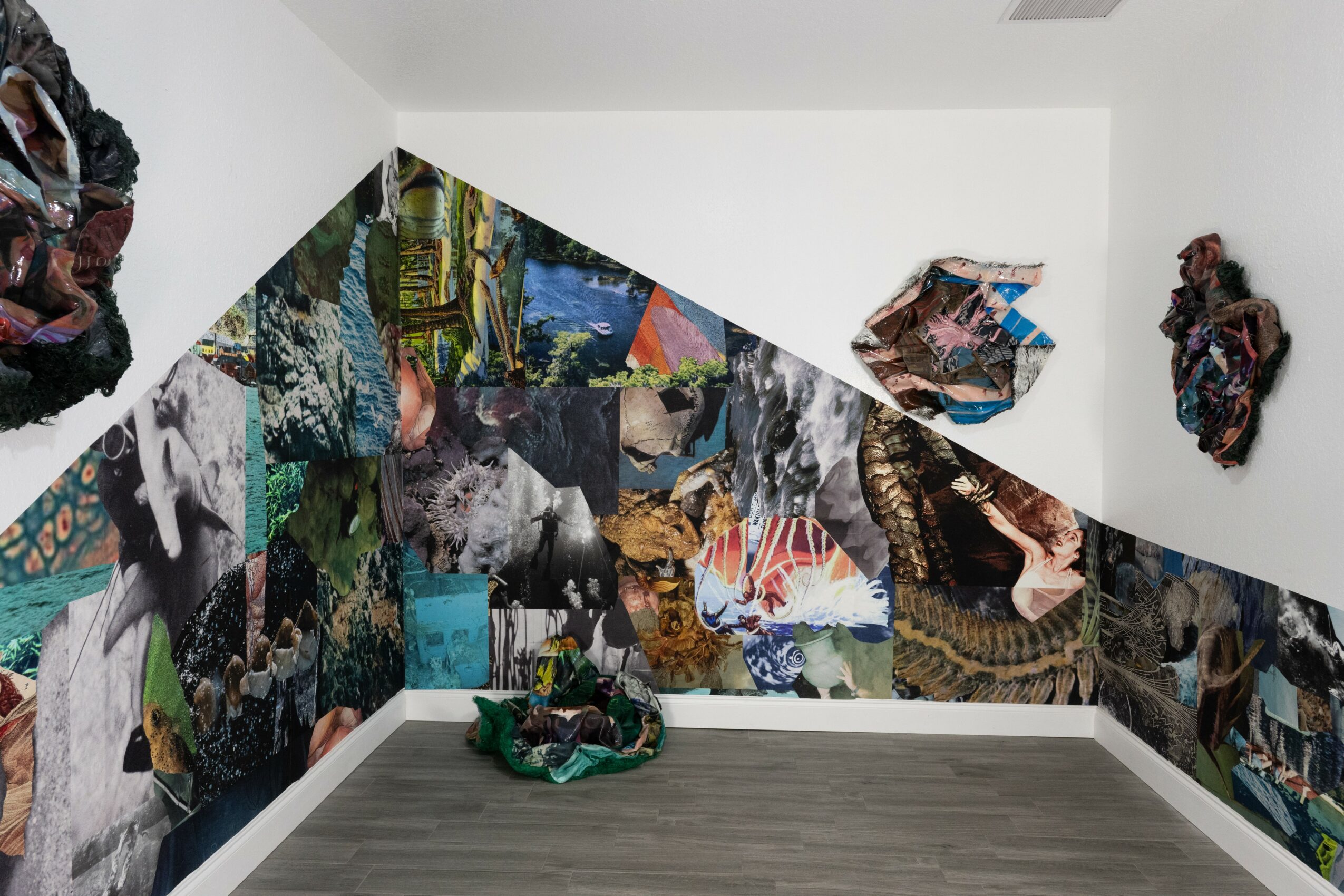 Gallery corner with collage artwork on walls and floor, featuring various images and textures, in a white room.