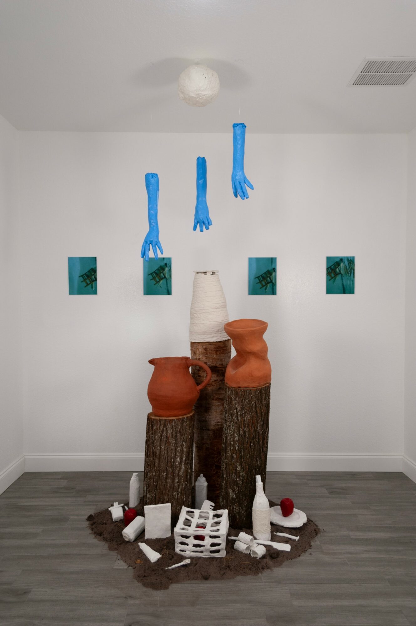 Decorative display with clay pots, wooden logs, and small objects on a circular base against a white wall with framed pictures.