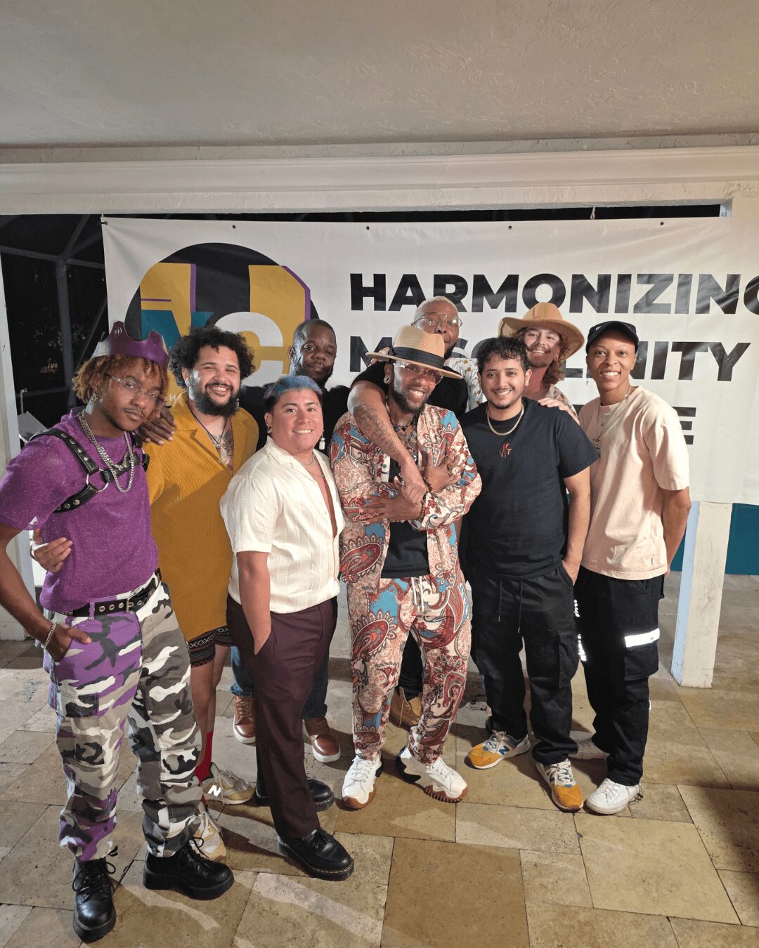 Group of seven diverse people standing together indoors, smiling, in front of a banner with text and graphics.