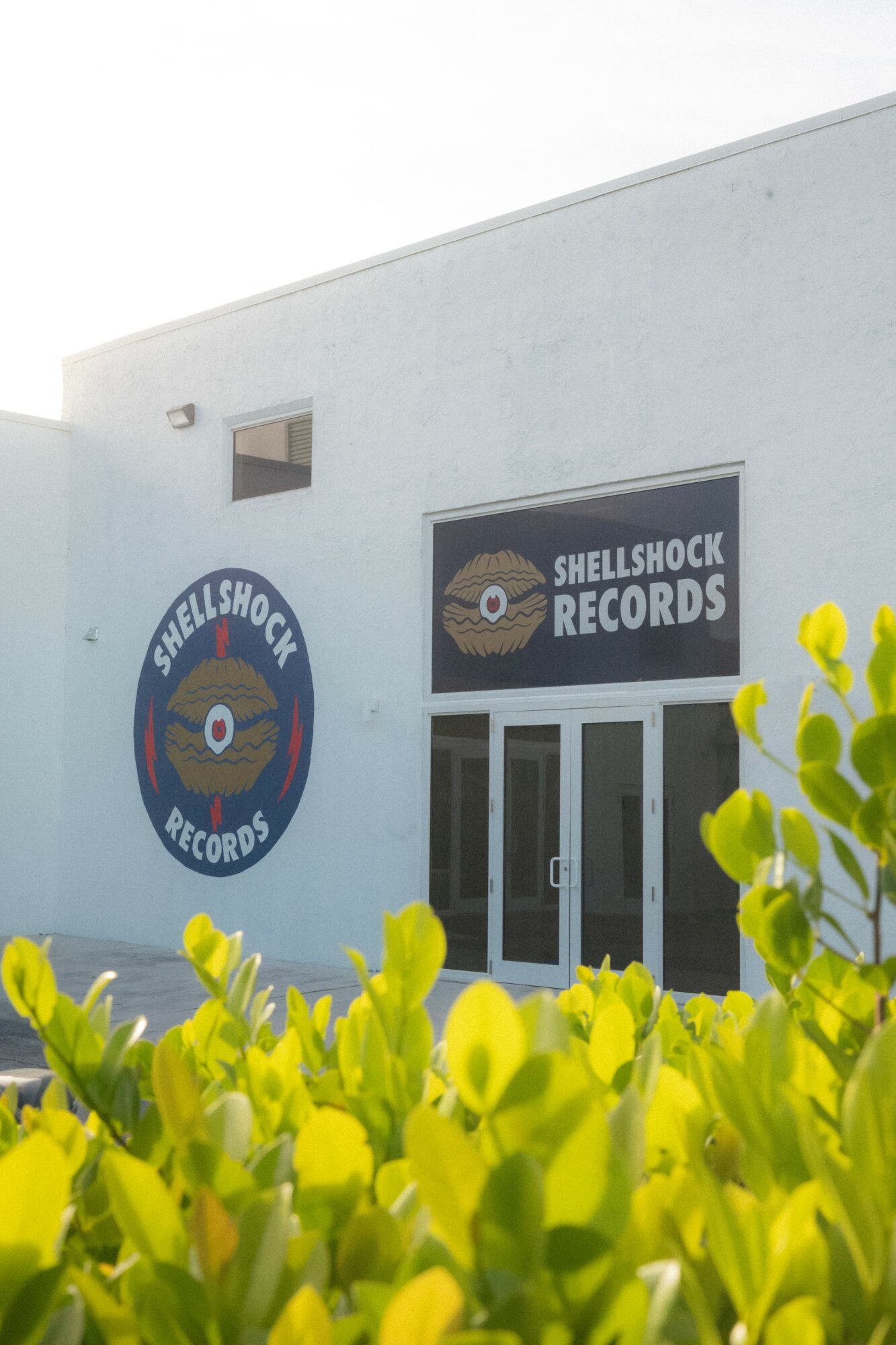 Building with Shellshock Records signs, surrounded by green plants, under a clear sky.