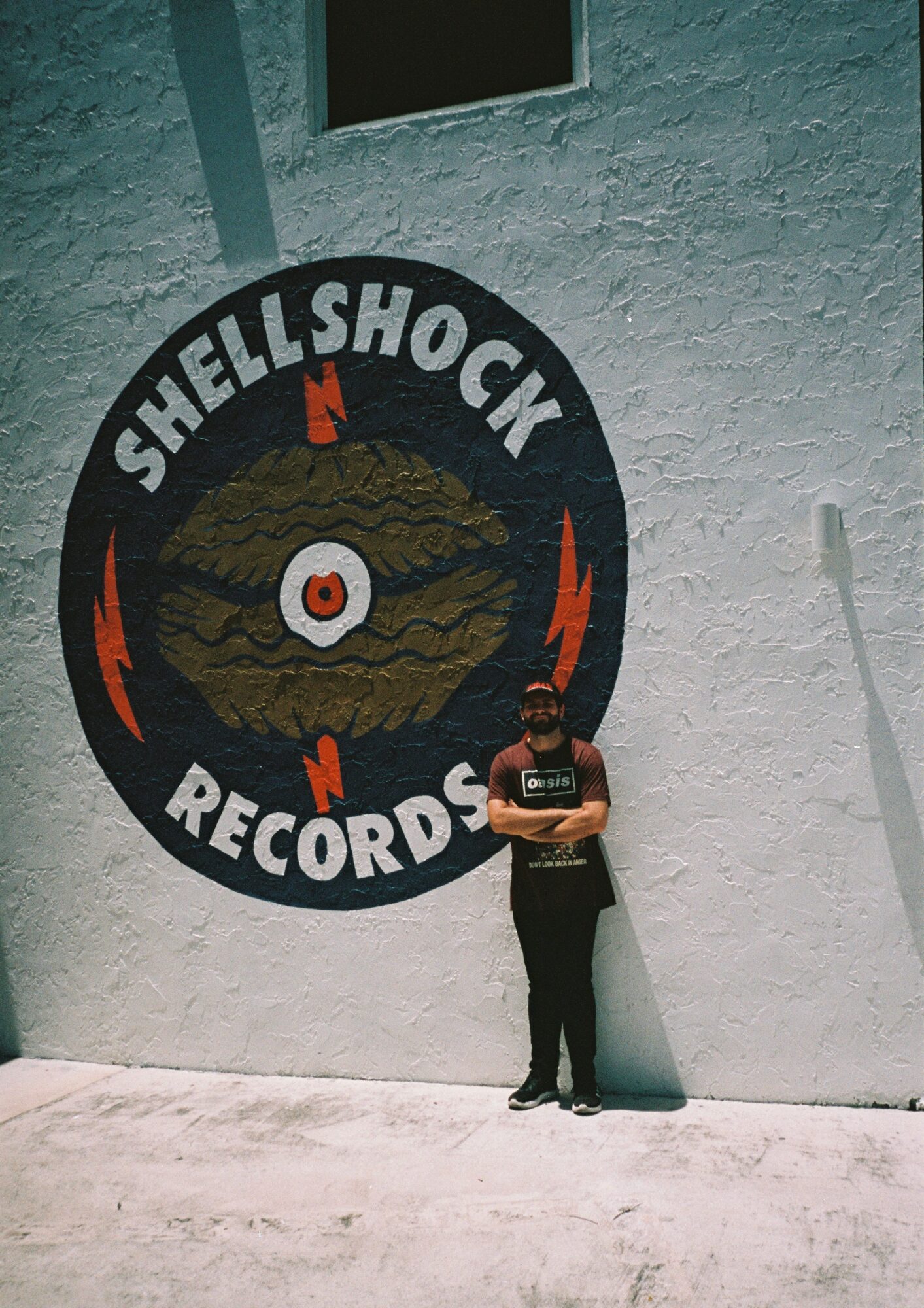 Person standing against a white wall with a Shellshock Records logo featuring a record and flames.