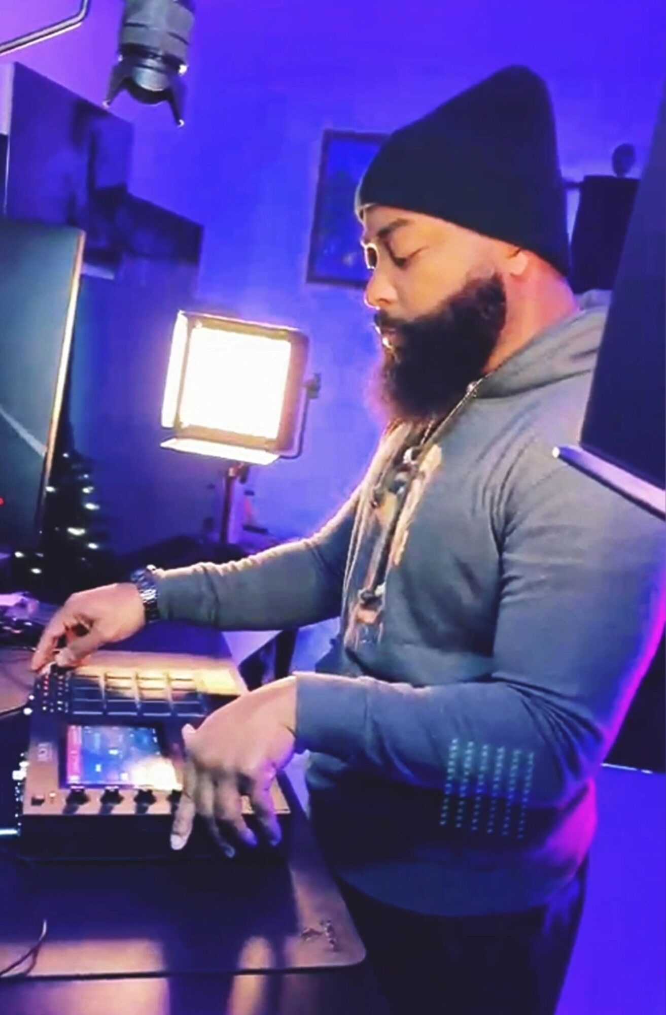 Person with a beard and beanie using music equipment in a dimly lit room with blue lighting.