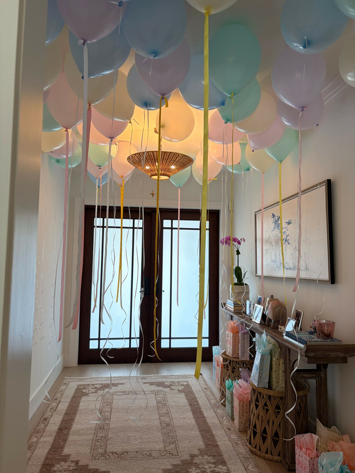 Room decorated with pastel balloons, a window with curtains, and a table with chairs, viewed from the side.