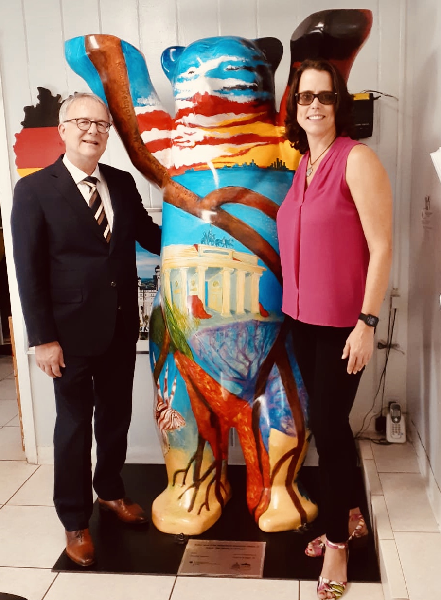 Two people standing next to a colorful, abstract sculpture of a dog, smiling indoors.