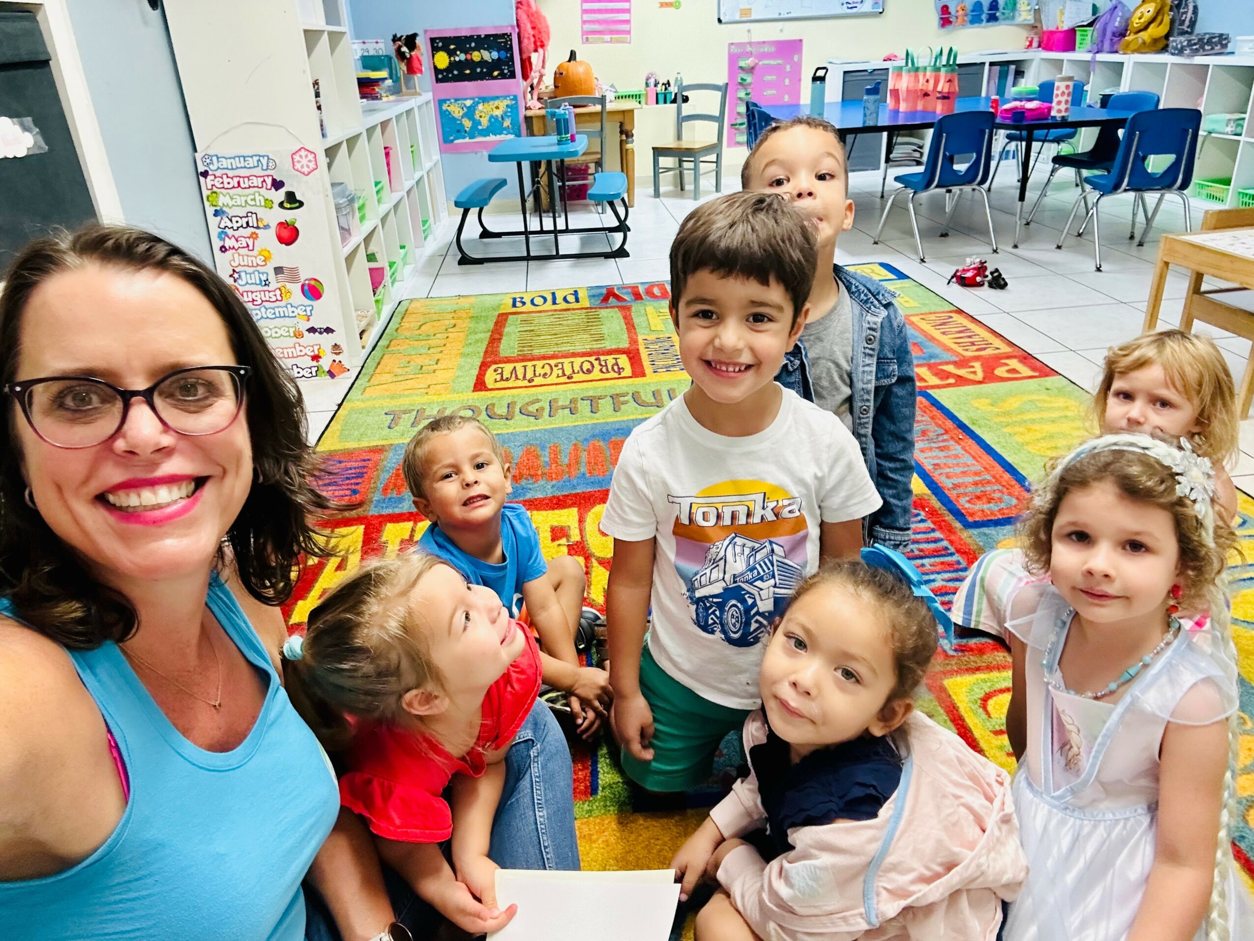 A teacher and six children in a colorful classroom, smiling and posing for a photo.