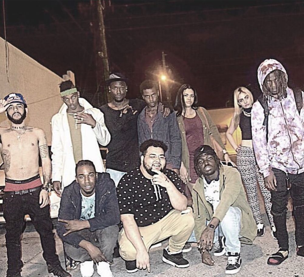 Group of ten diverse young adults posing outdoors at night, some standing and some crouching, with streetlights in background.