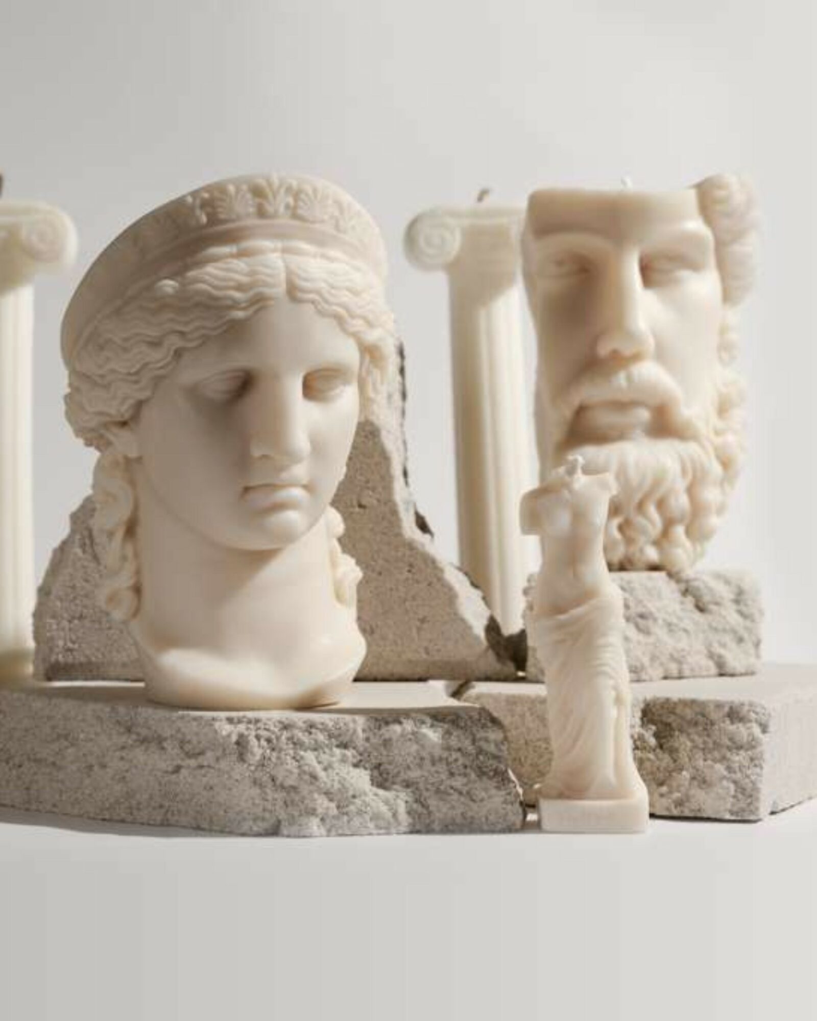 Broken classical sculpture busts of a woman and a man with a smaller figure in front, all on a white surface.