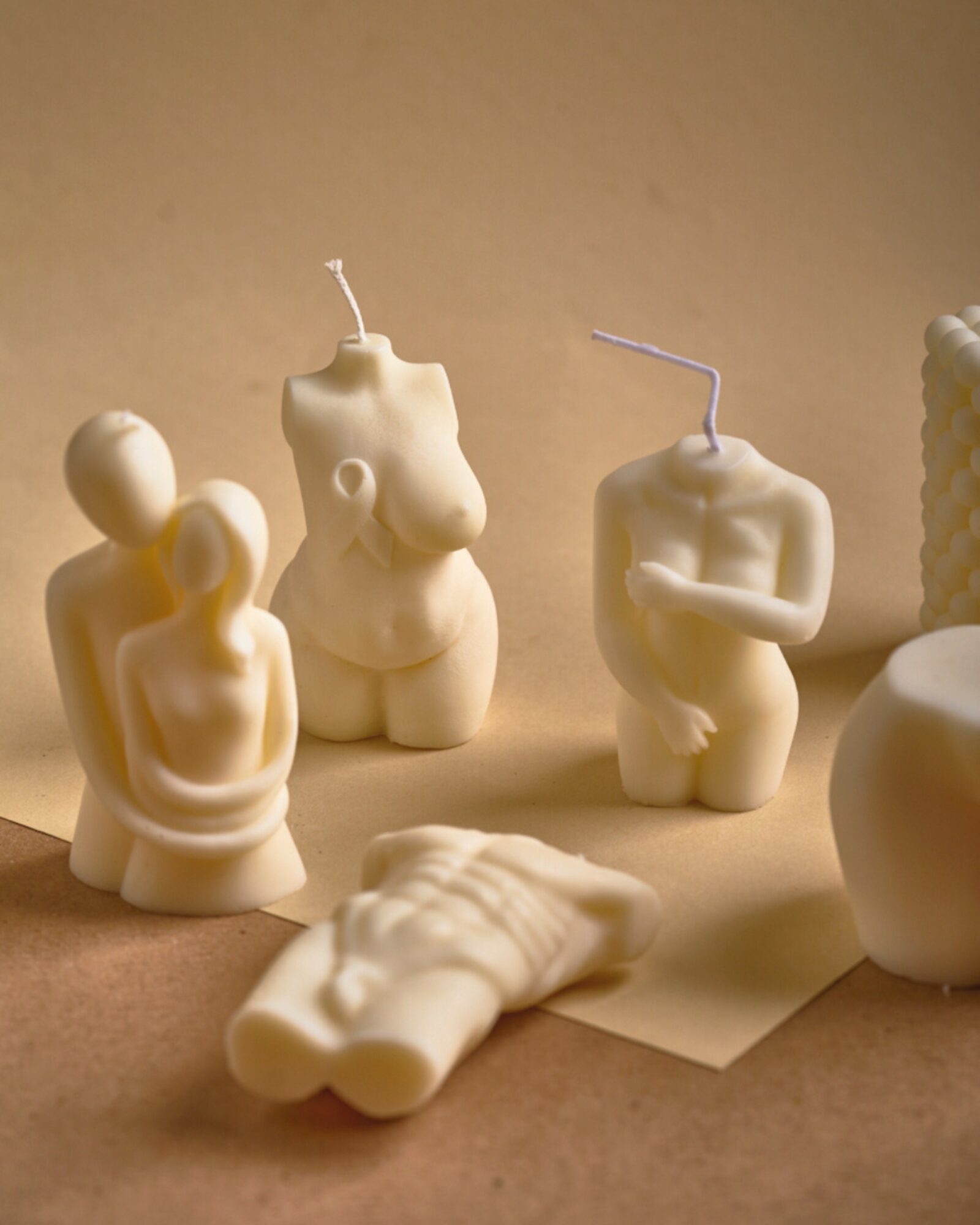 Several unlit candles shaped like human figures and objects on a beige surface, with a plain background.