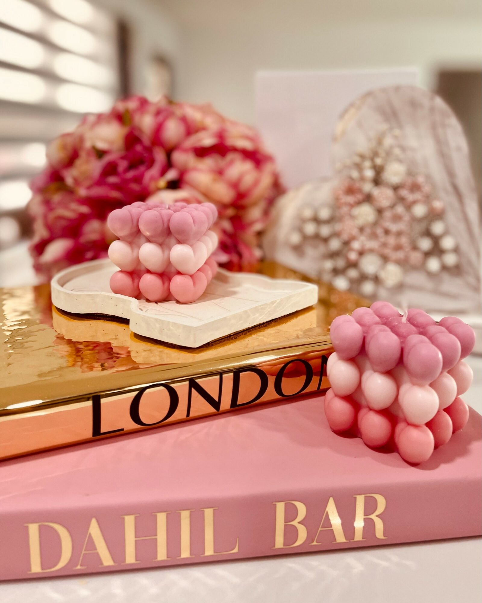 Decorative pink bubble-shaped candles on a pink and gold surface with a blurred floral background.